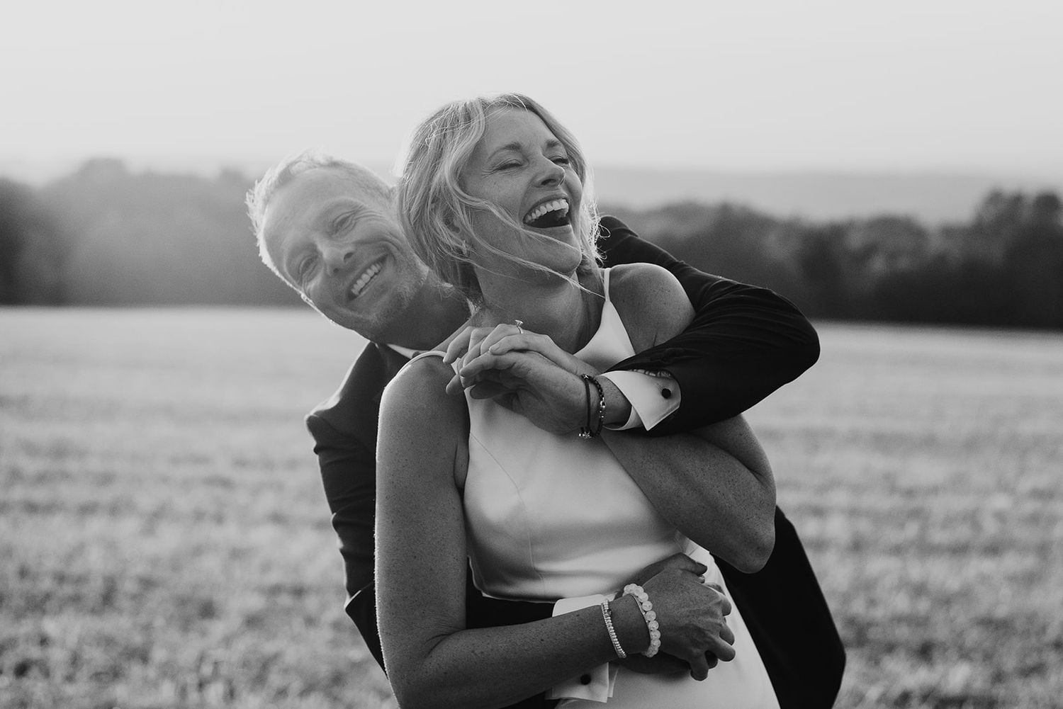Romantic black and white photo series of a couple embracing in a field at sunset.