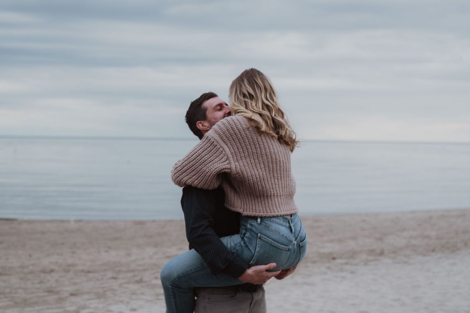 Romantic couple embracing on a beach with cloudy sky backdrop.