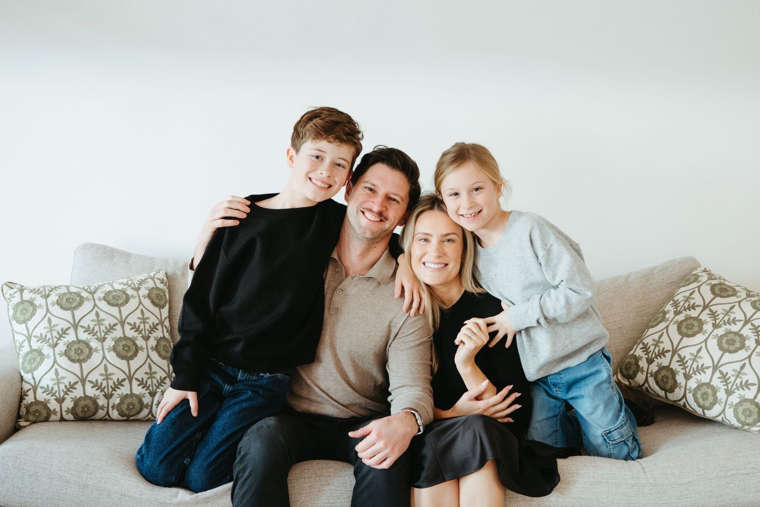 Happy family of four smiling together on a cozy couch, featuring two parents and two children in a bright living room.