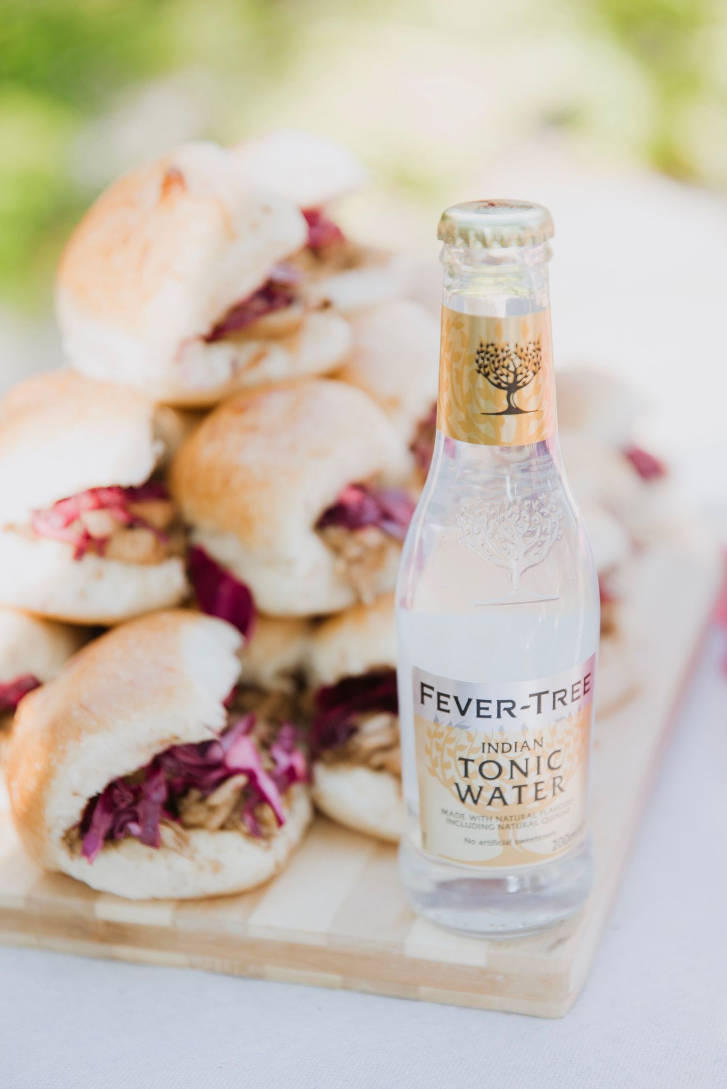 Fever-Tree Indian Tonic Water bottle beside fresh mini sandwiches with red cabbage filling on a wooden board.