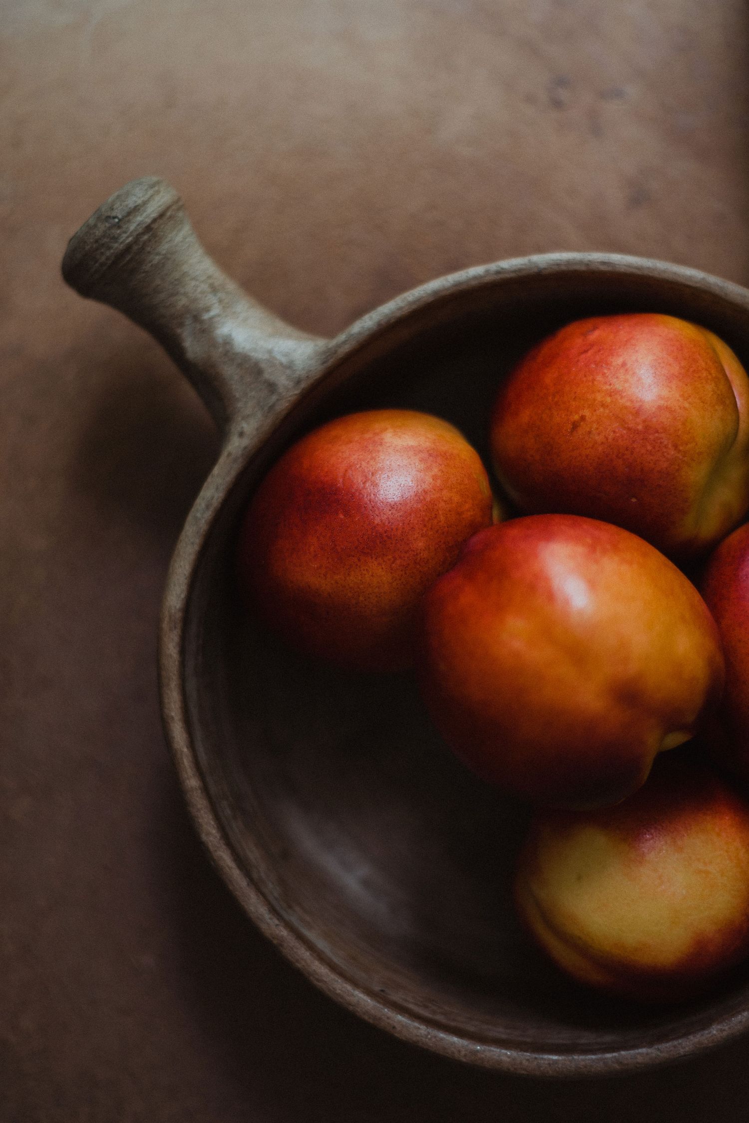 Ripe nectarines in a rustic wooden bowl with handle on dark brown surface.