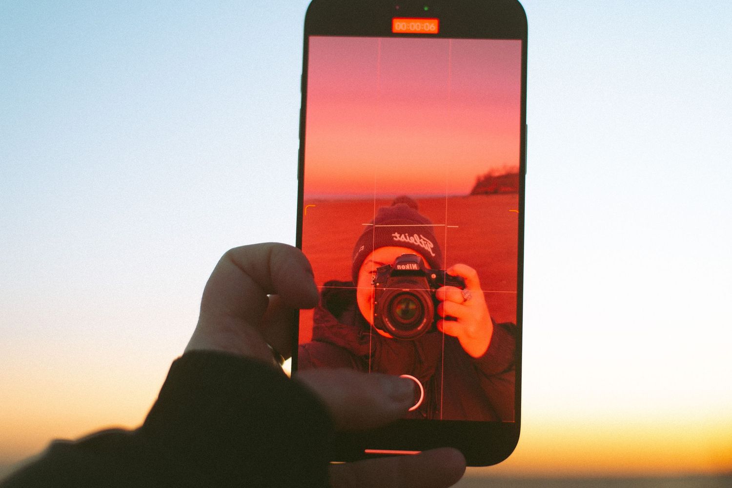 Phone screen showing sunset reflection with camera lens in frame.