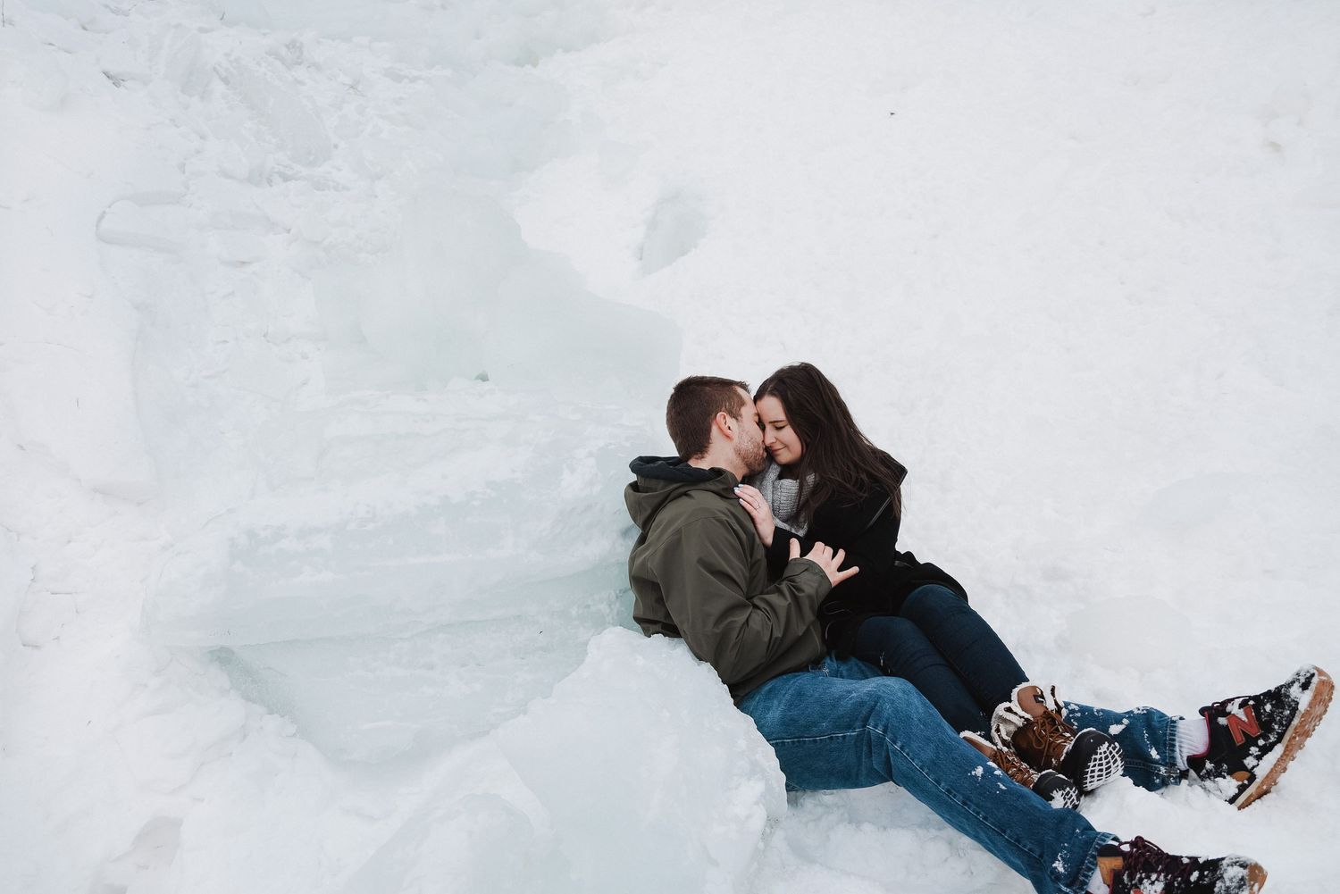 Couple sitting together in snow, sharing a romantic moment outdoors in winter, wearing casual jackets and jeans.