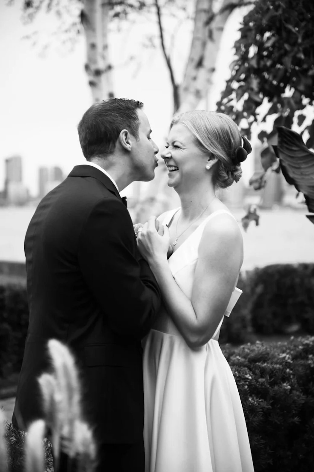 Black and white wedding photo of smiling bride and groom sharing a romantic moment outdoors near a waterfront.