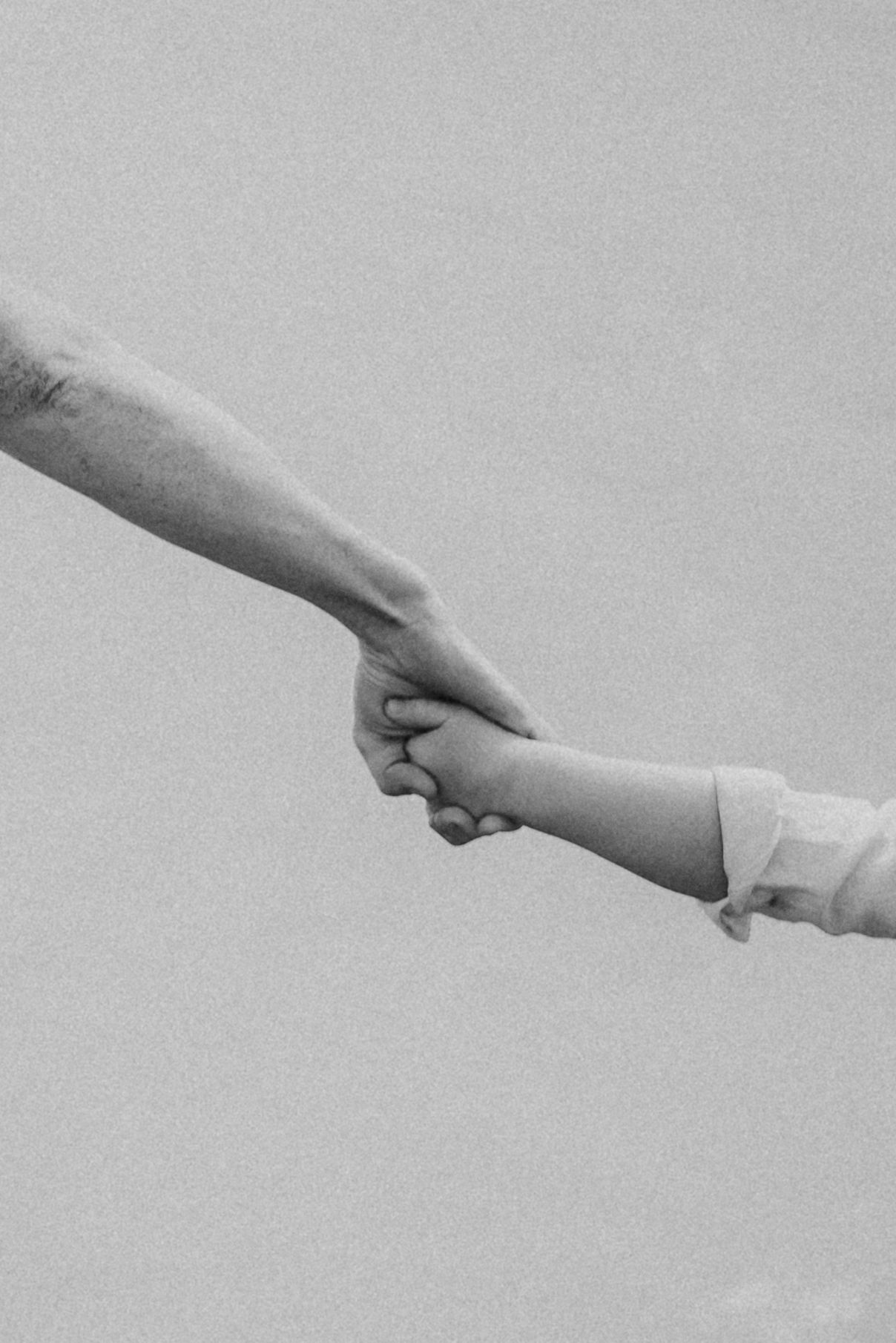 Black and white photo of an adult and child holding hands, symbolizing love, trust, and family connection.