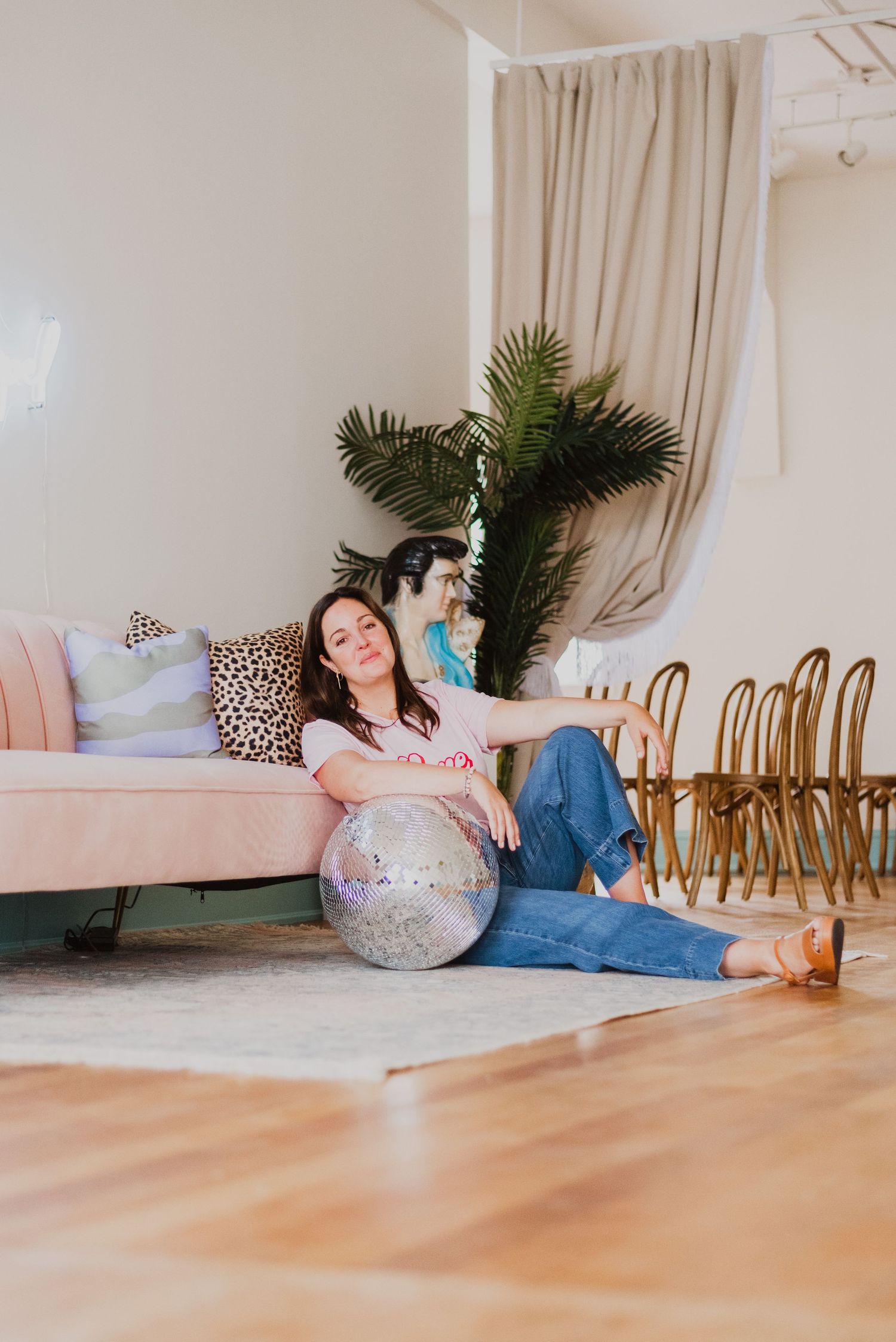 Woman sitting on floor leaning against pink sofa with disco ball in bright modern living room.