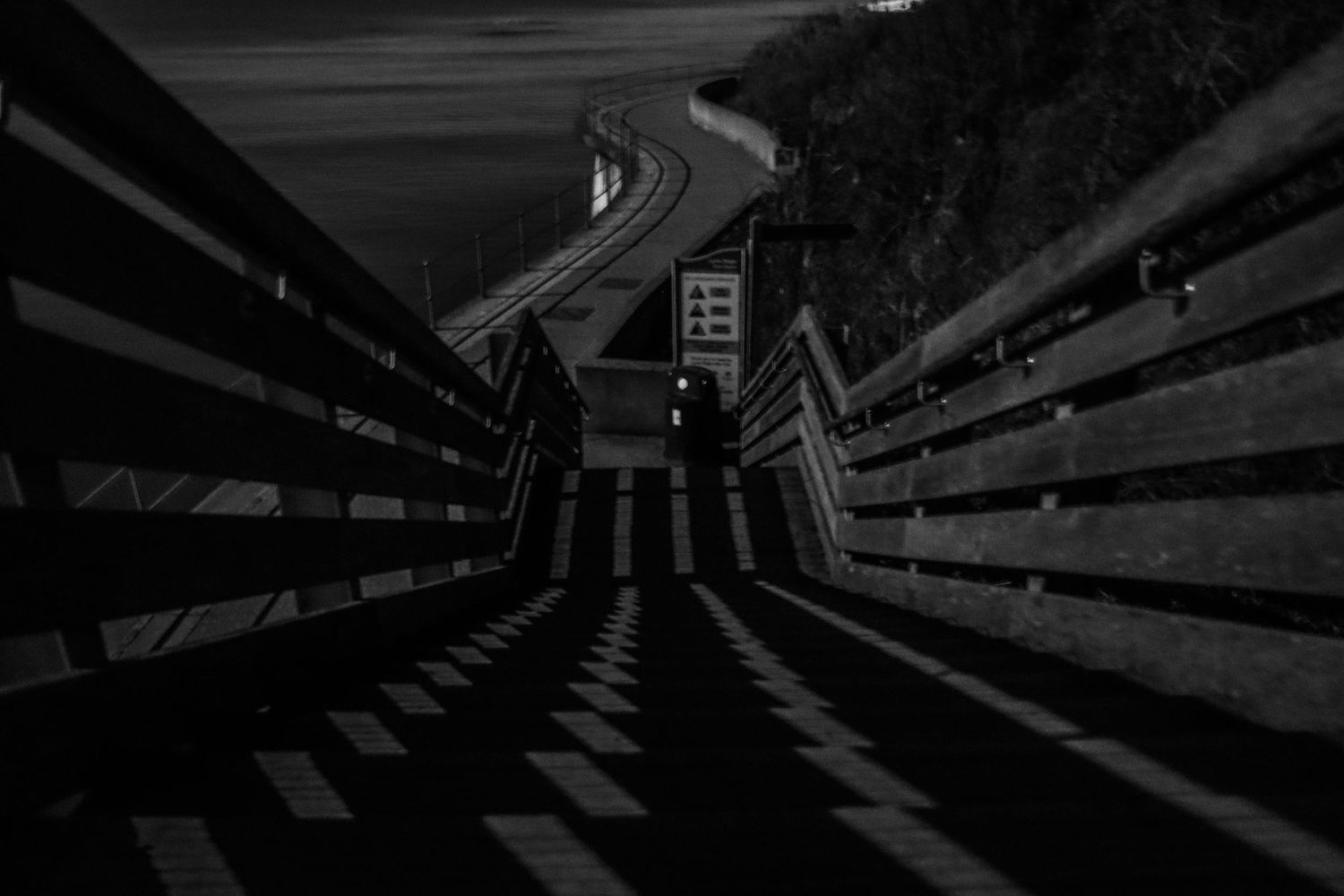 Dramatic black and white shot of wooden boardwalk steps leading to a winding road at night.