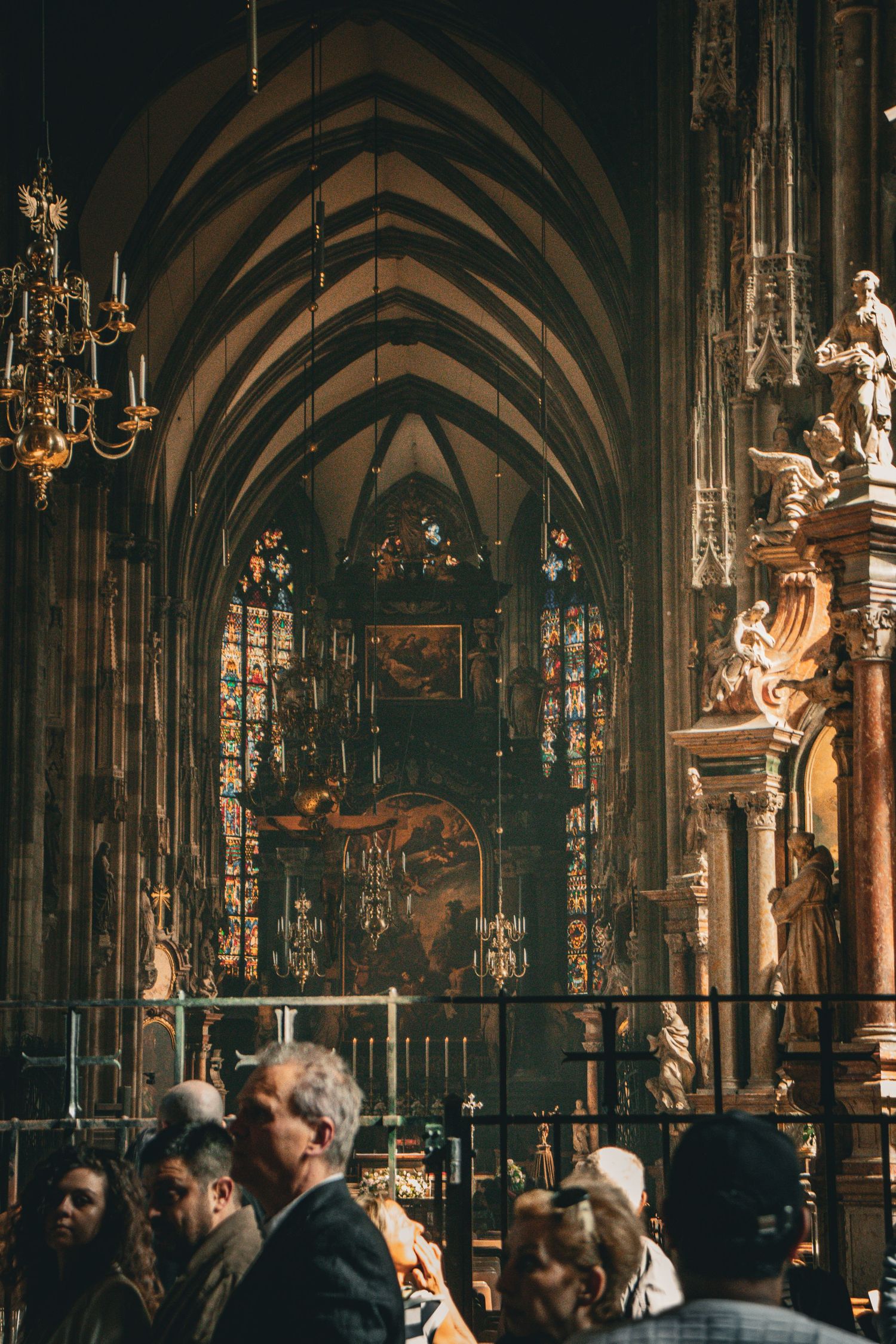 Visitors inside a grand Gothic cathedral with ornate stained glass windows and vaulted stone ceiling.