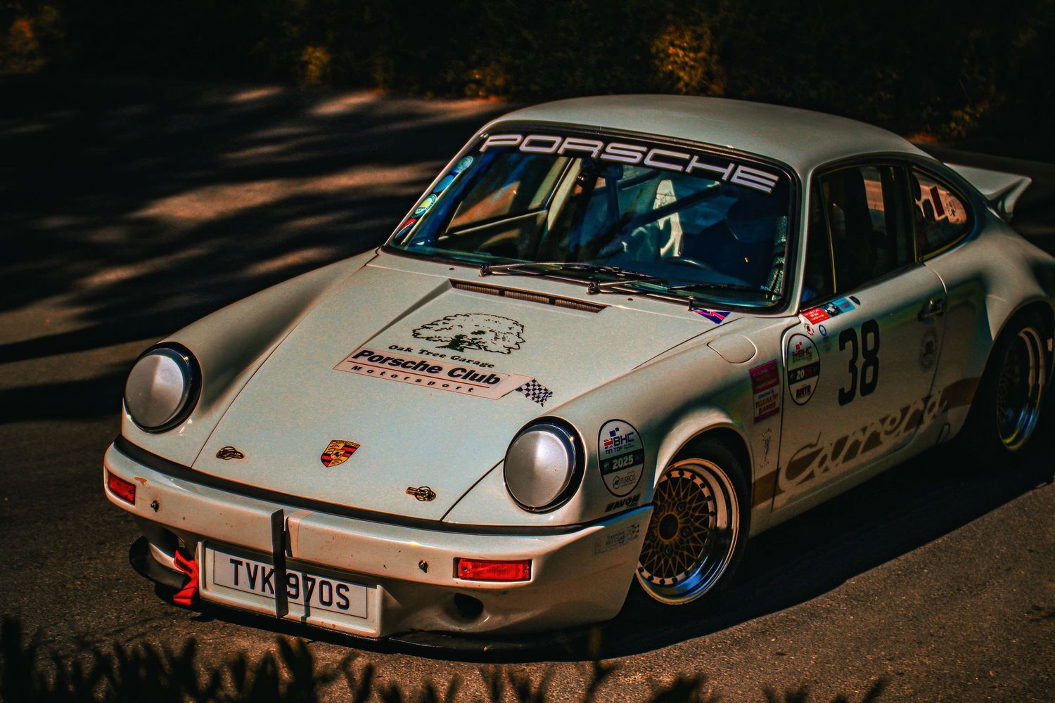 A vintage white Porsche 911 race car number 38 parked on a sunlit road.