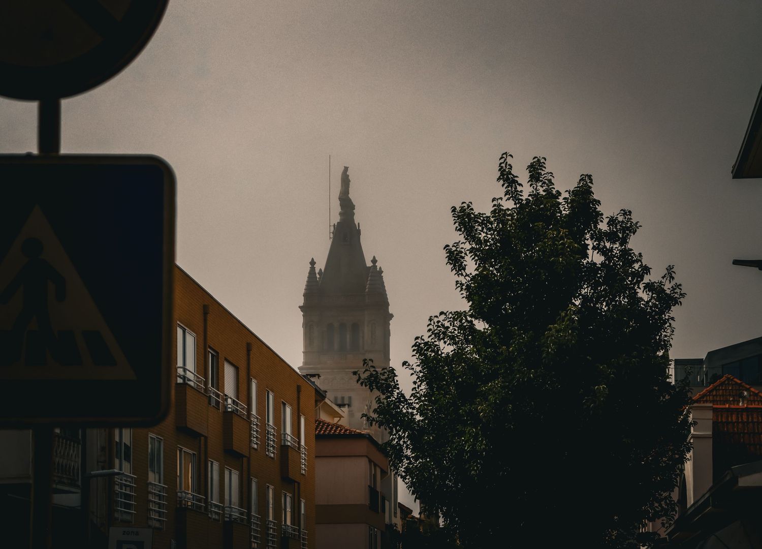 Dark stormy sky over city buildings with a historic church tower and tree silhouette.