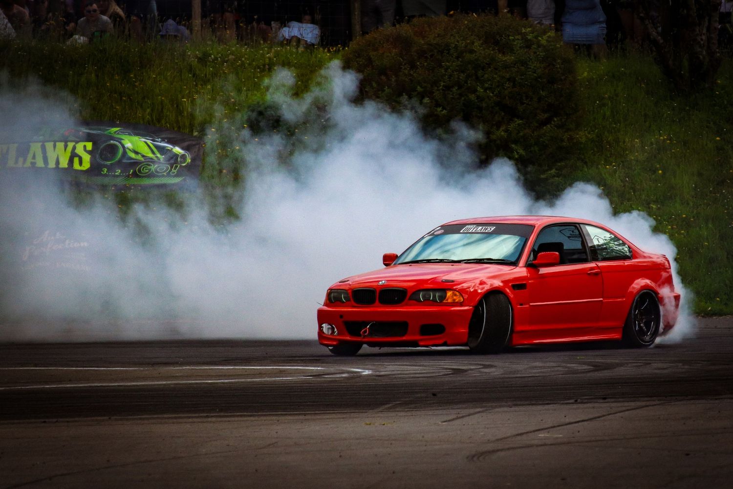 Red BMW M3 drifting with heavy white smoke on a motorsport track.