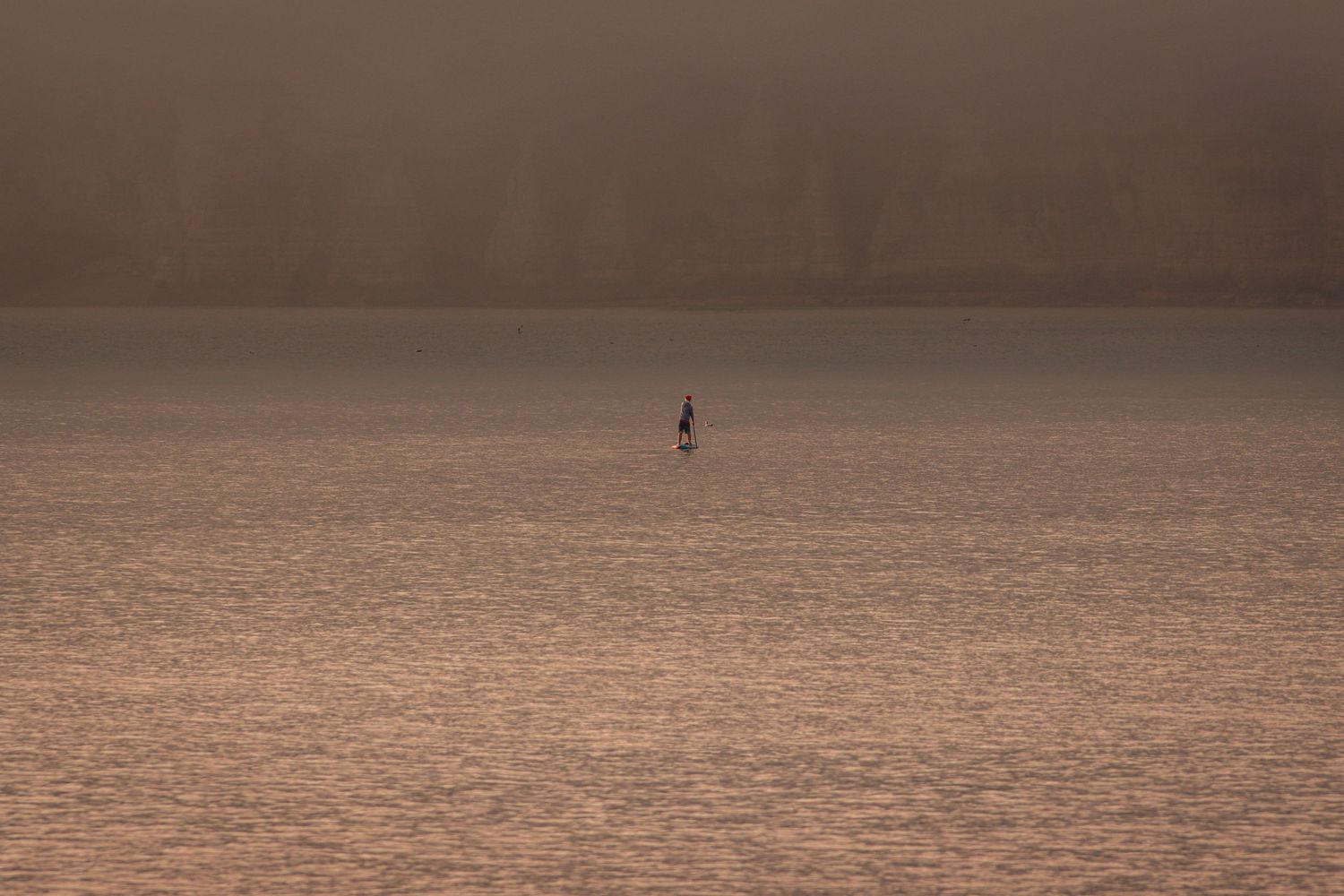 Lone sailboat on calm misty water at sunset.