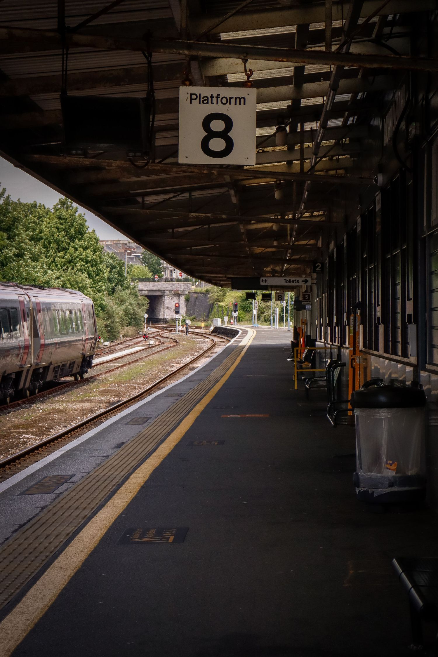 Empty Platform 8 at a train station with a passenger train visible on the tracks under a covered platform.
