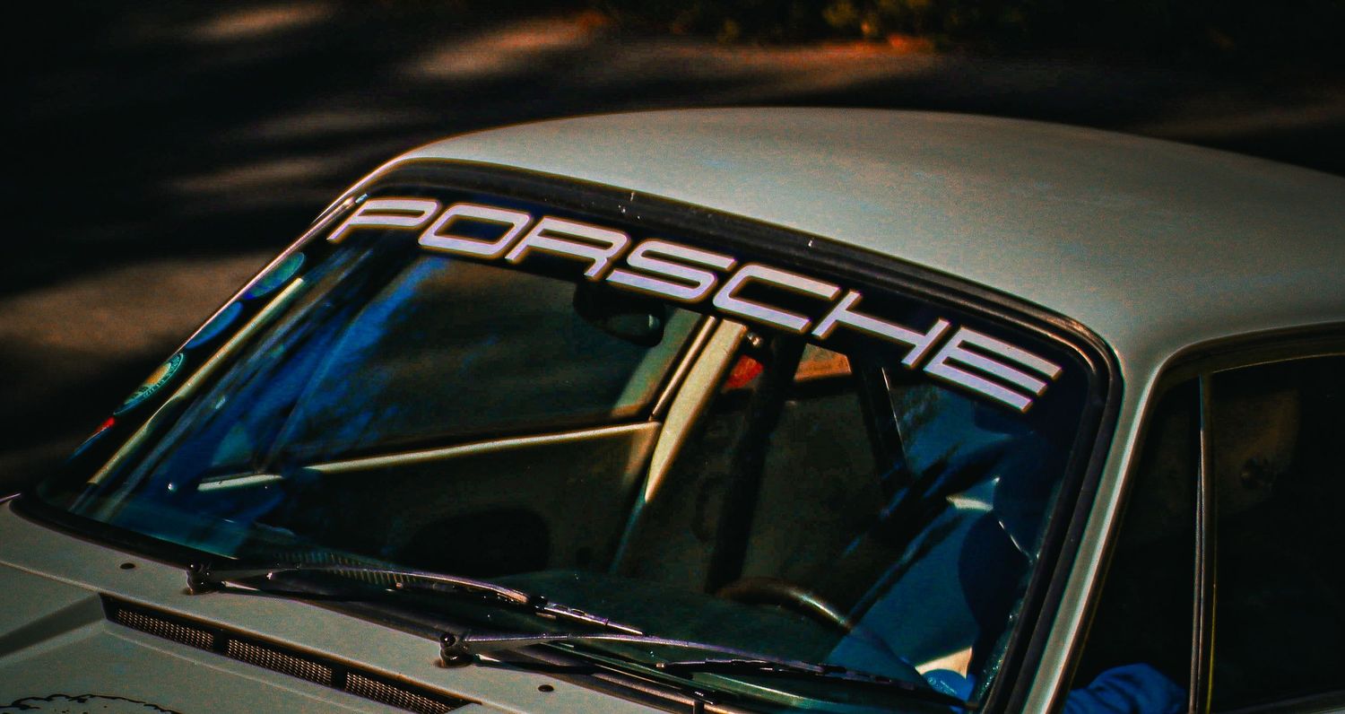 Close-up of a Porsche windshield banner on a classic white sports car.