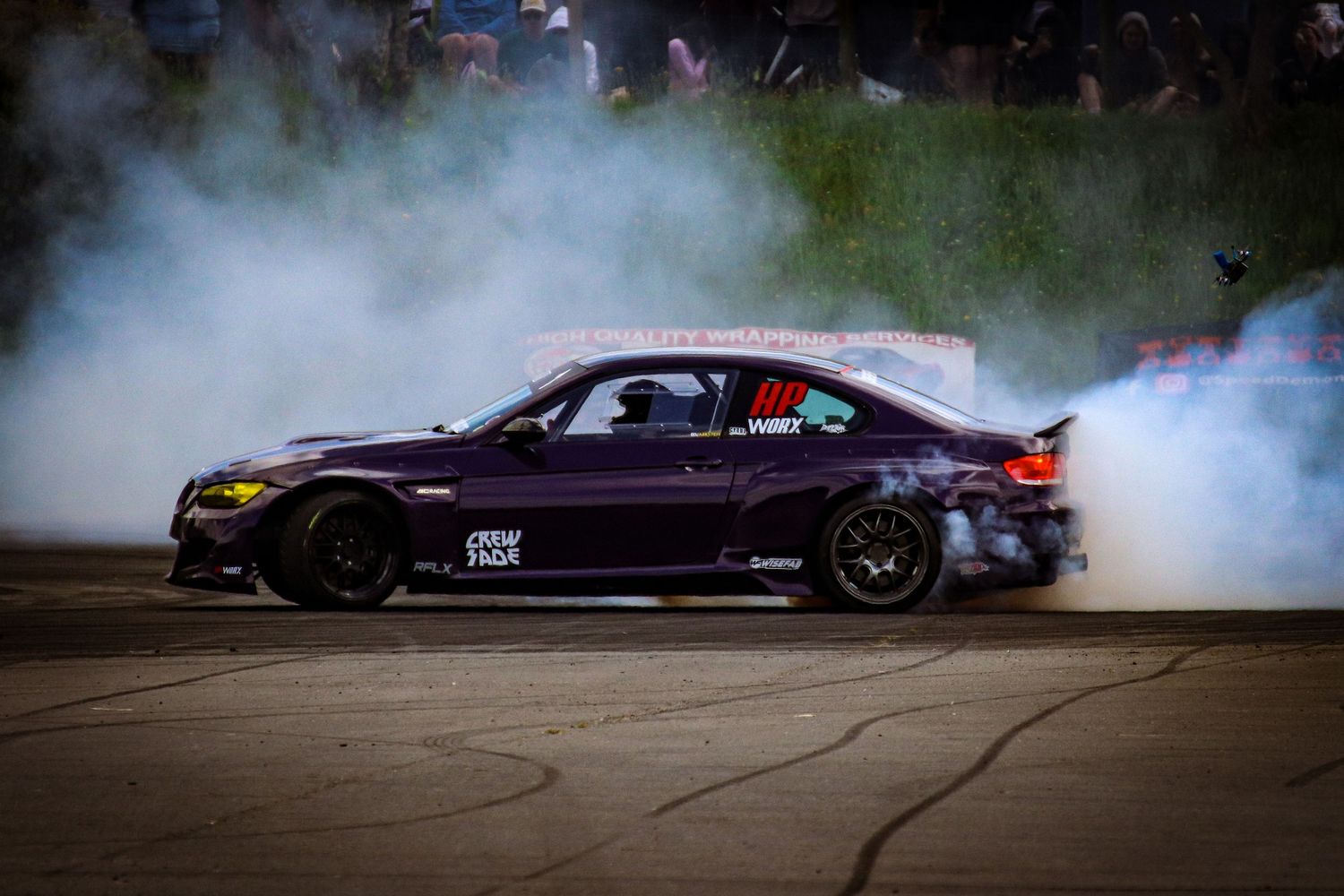 Purple BMW drifting on a track surrounded by smoke at a motorsport event.