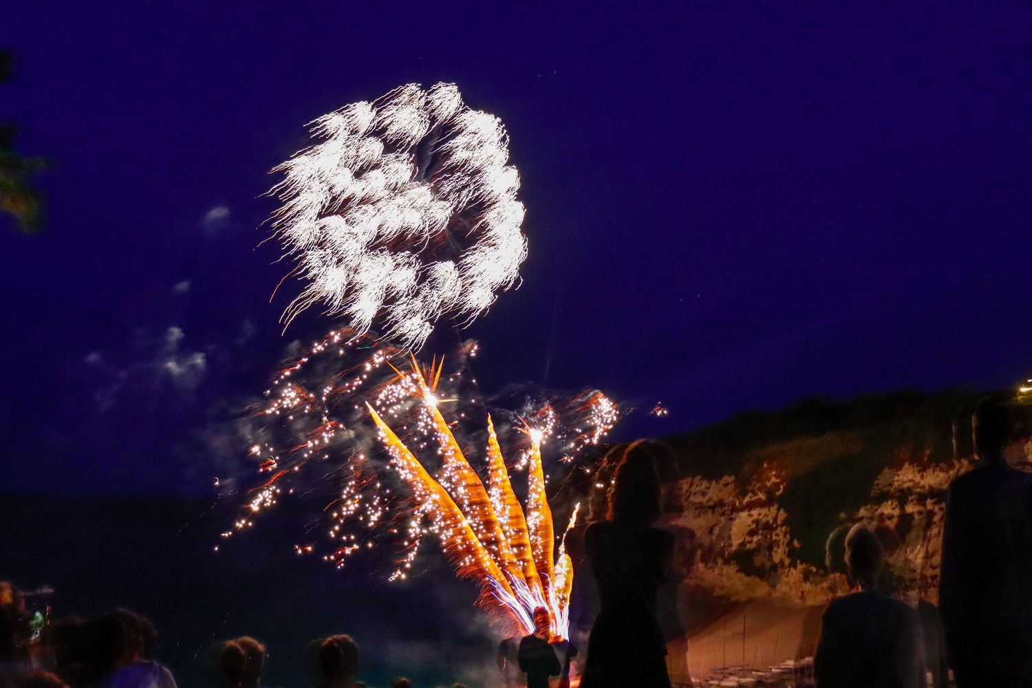 White fireworks burst against a dark blue night sky above a crowd of spectators.