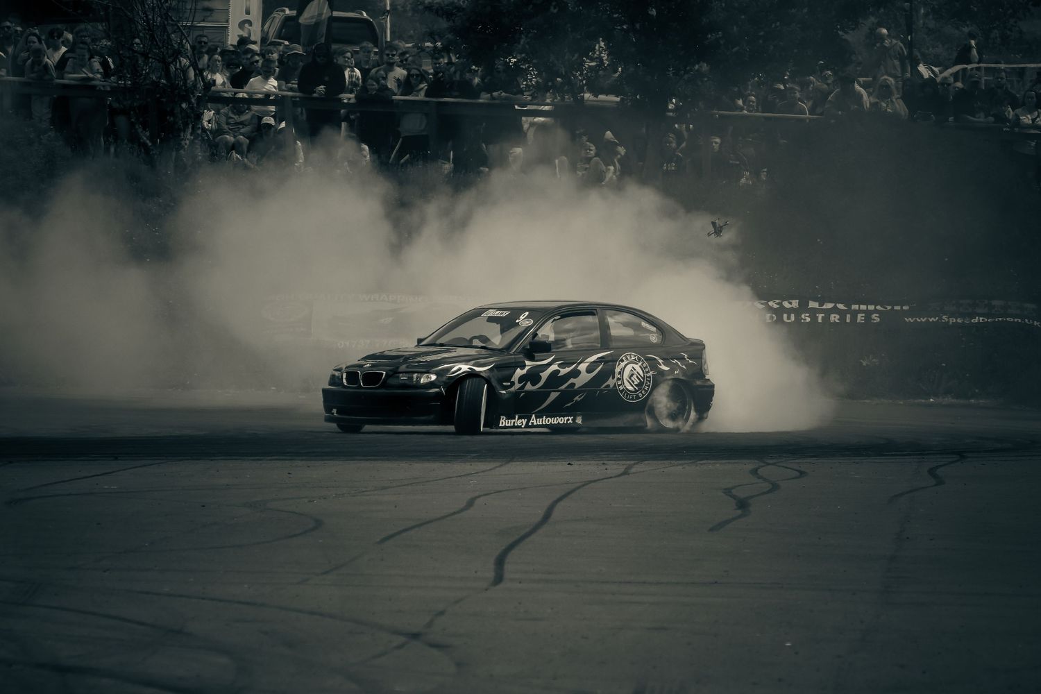 Black and white photo of a BMW drifting with heavy smoke at a motorsport event.