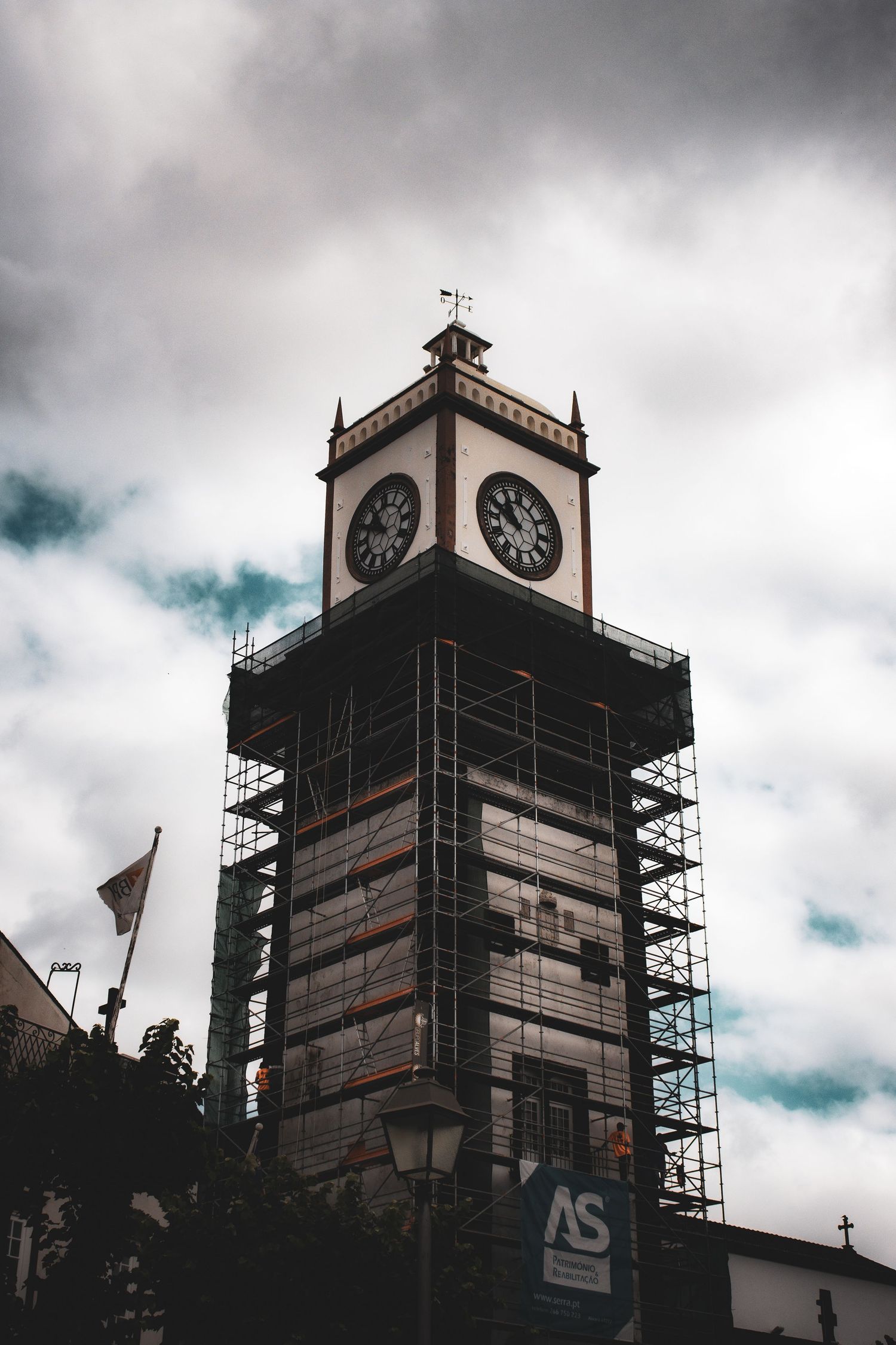 A historic clock tower undergoing renovation is surrounded by metal scaffolding under a cloudy sky.