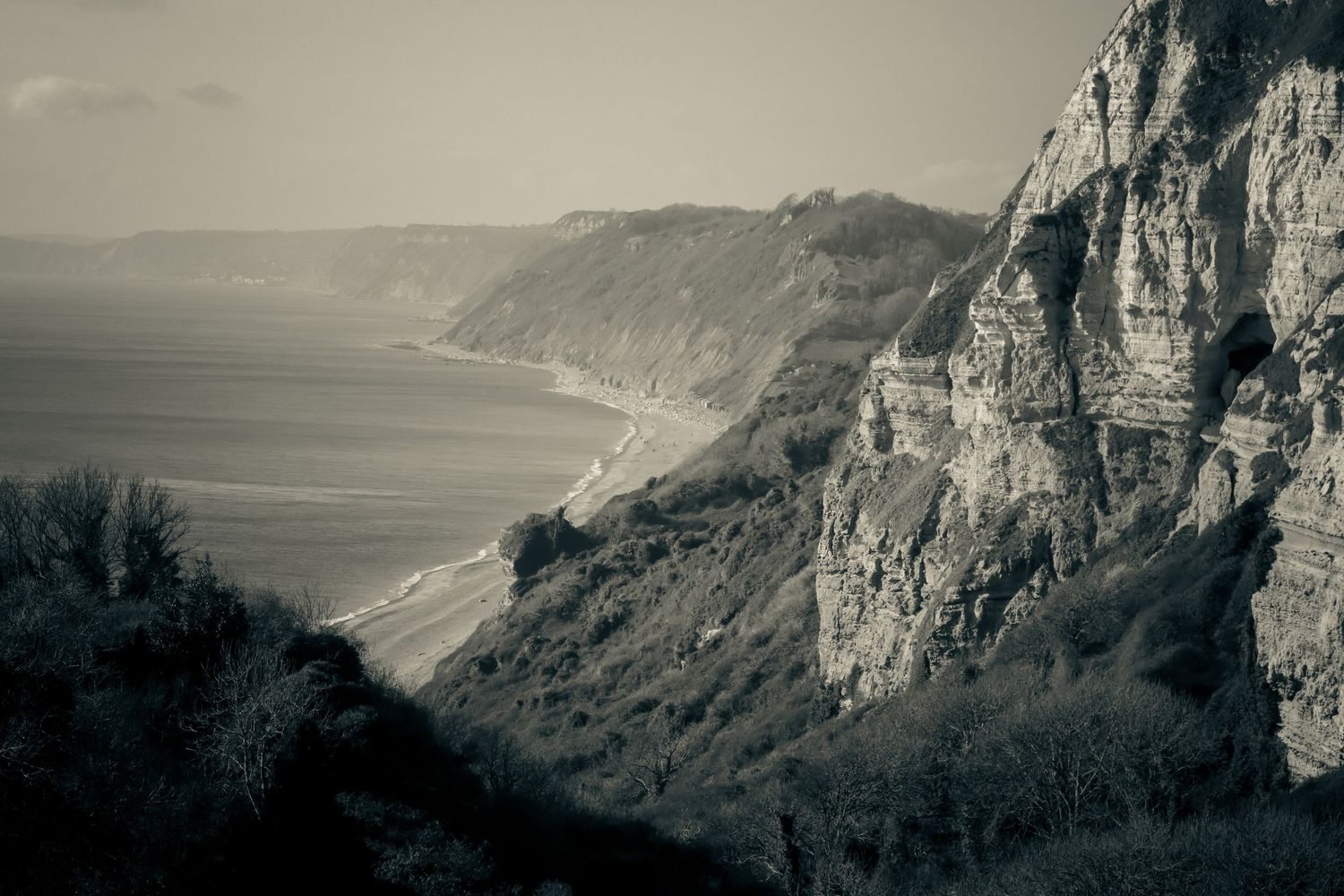 Black and white aerial view of dramatic coastal cliffs and shoreline stretching into the distance.
