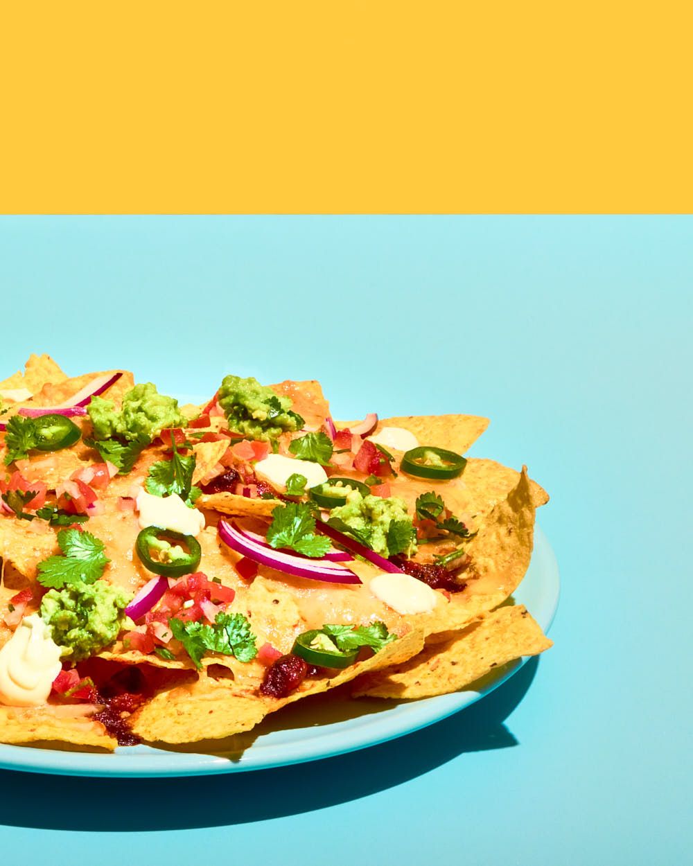 Plate of colourful nachos on yellow and turquoise background