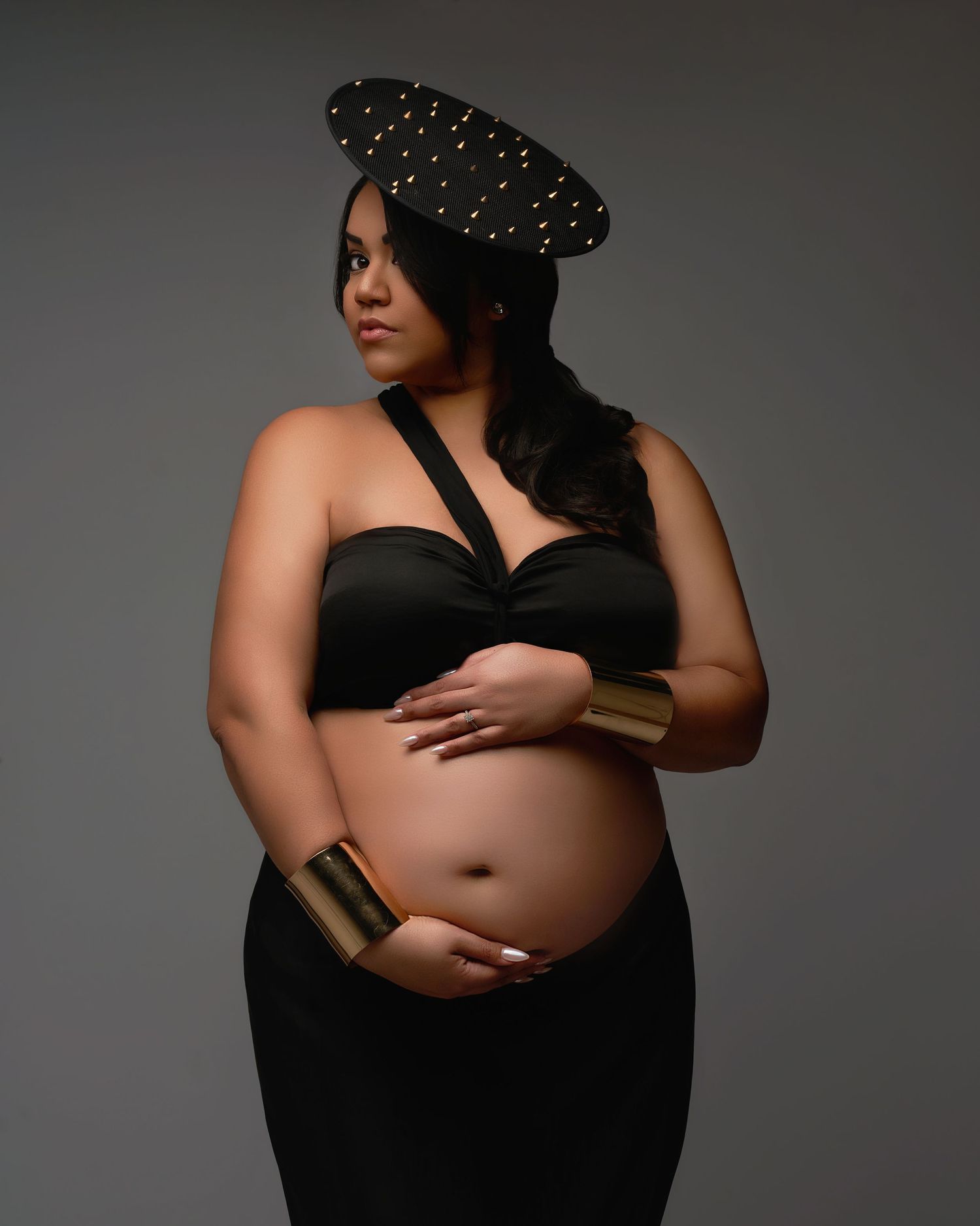 Artistic maternity photo featuring a studded black beret and black dress against a gray backdrop.
