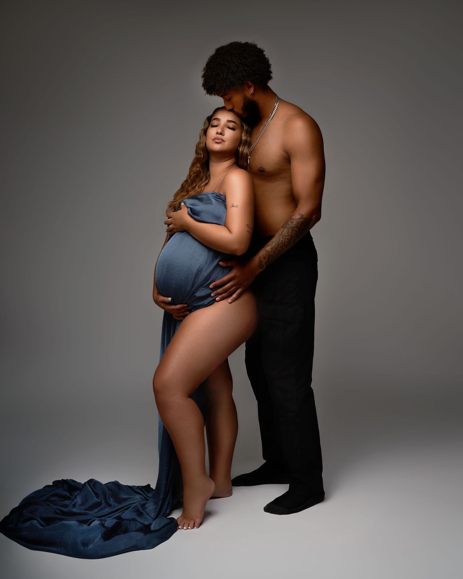 Intimate maternity photography session with couple in dark studio setting.