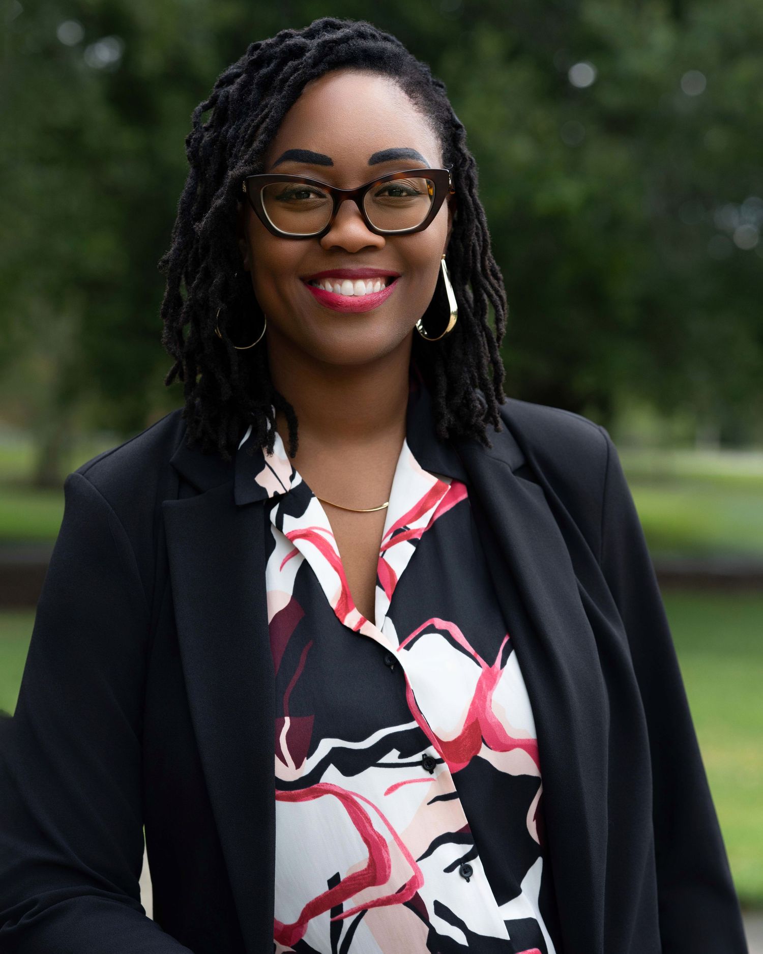 Outdoor professional portraits of a woman in a black blazer and patterned blouse.