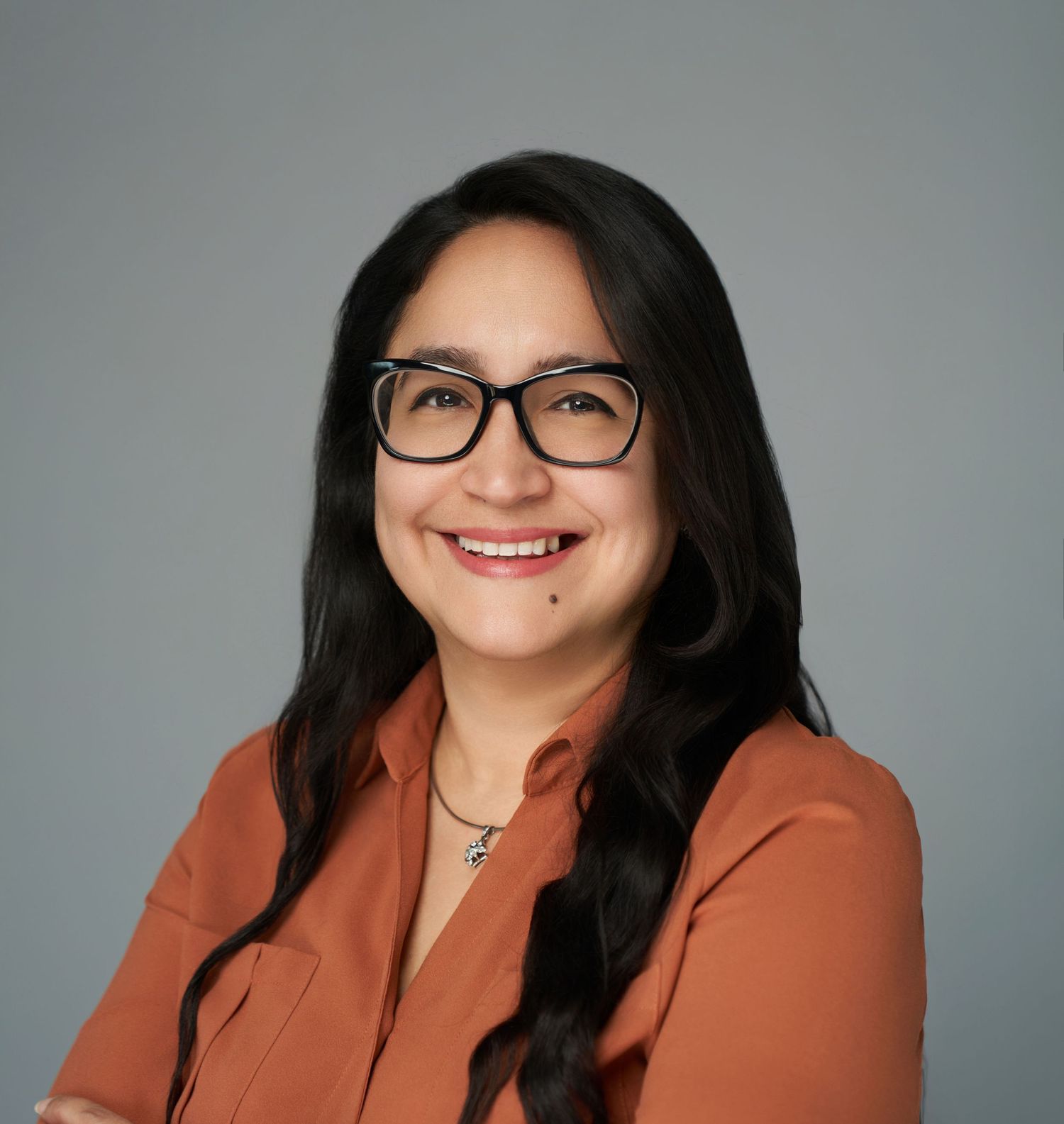 Professional headshots in rust-colored blazer against gray background.