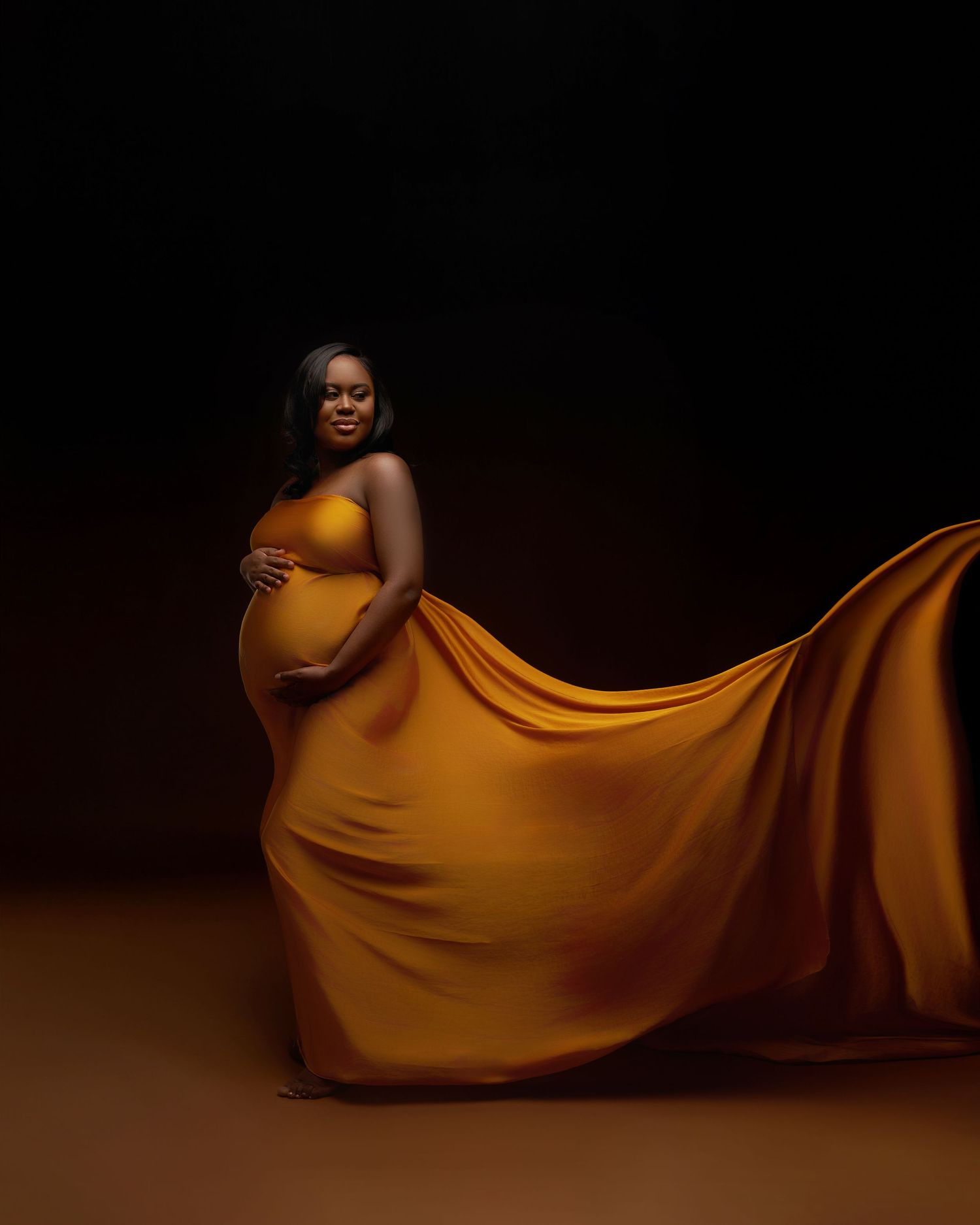 Dramatic maternity portraits in golden fabric with moody lighting creating artistic silhouettes.