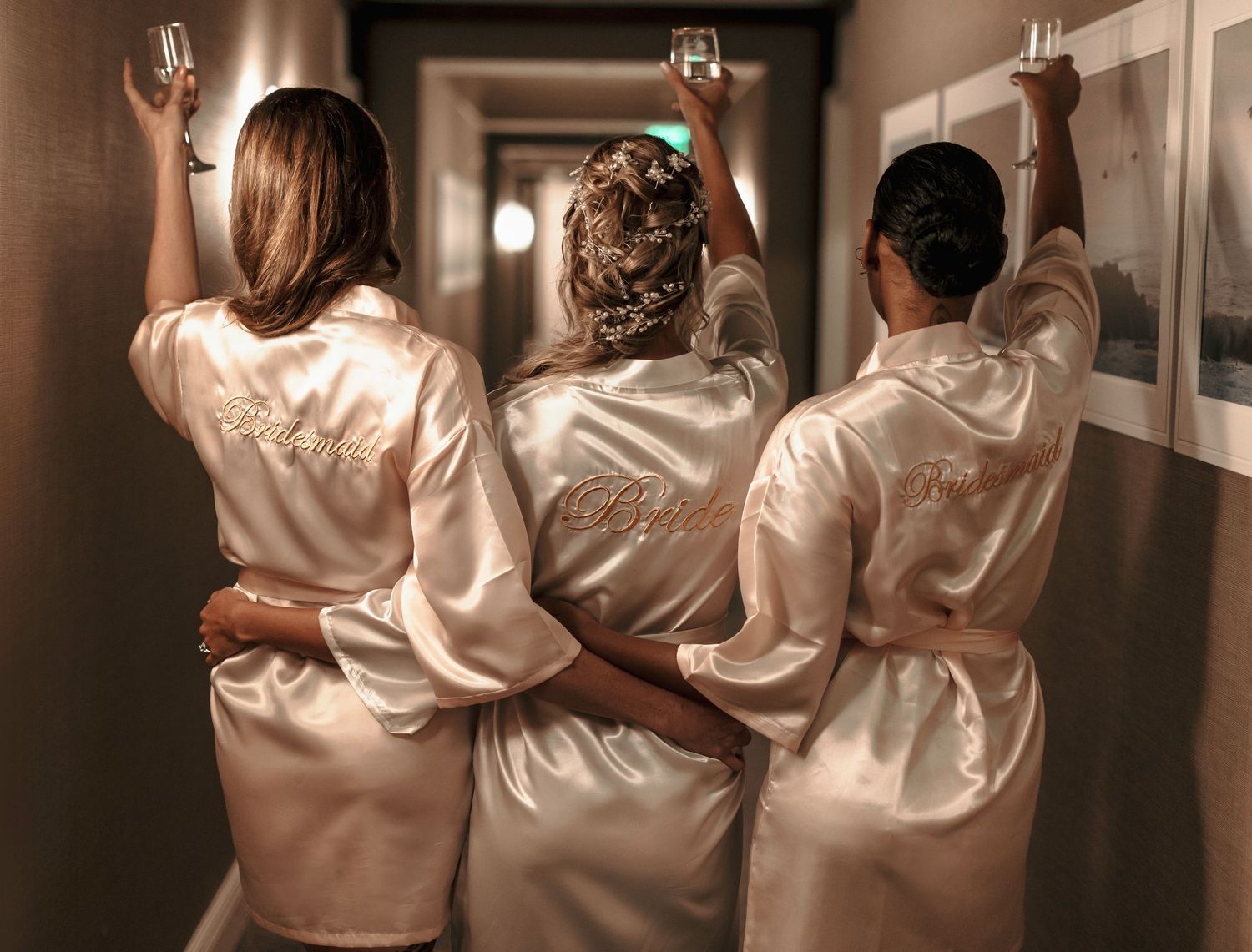 Group of women wearing matching silk bridal robes photographed from behind in a hallway.