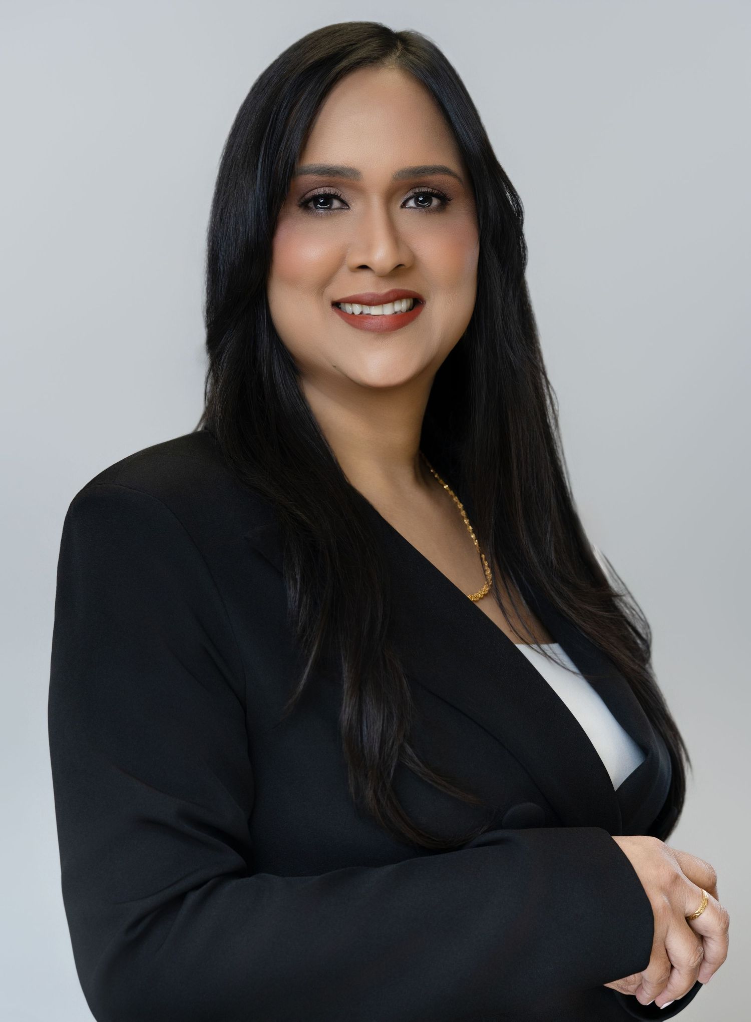 Professional headshot of a person in a black blazer smiling warmly against a light gray background.