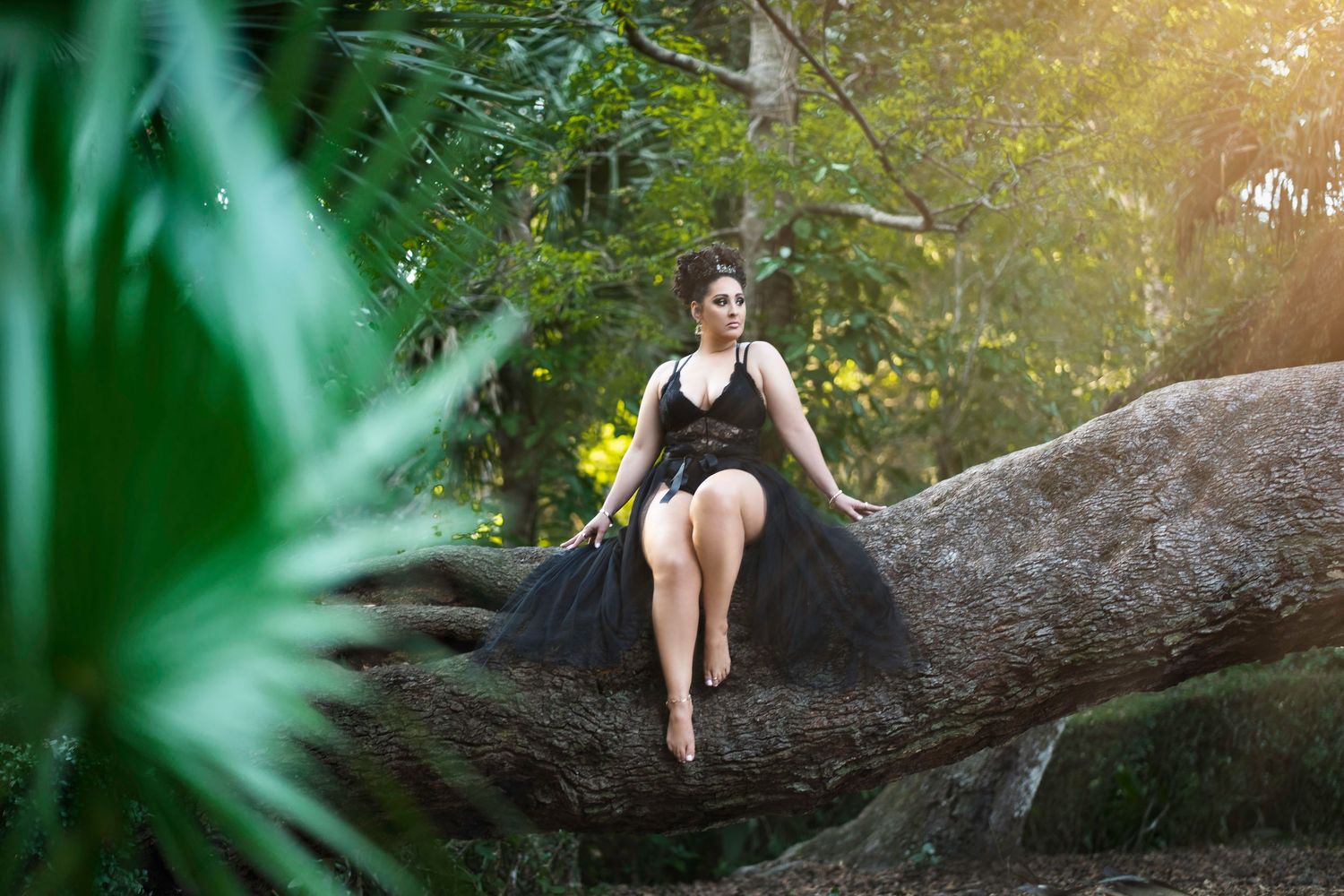A person in black athletic wear poses gracefully on a large fallen tree trunk in a lush tropical setting at sunset.
