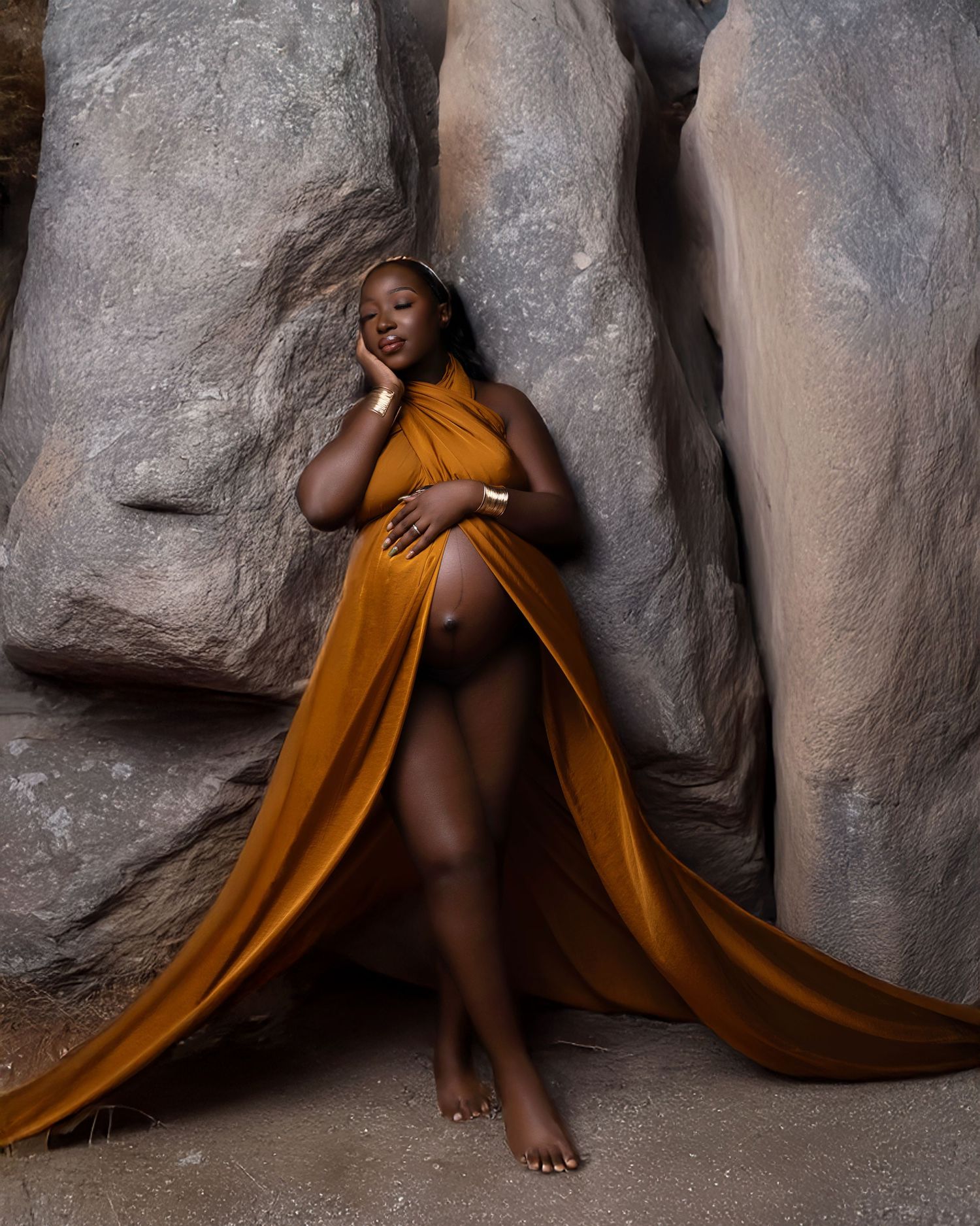 A model in a flowing mustard yellow dress poses elegantly against large gray rock formations.