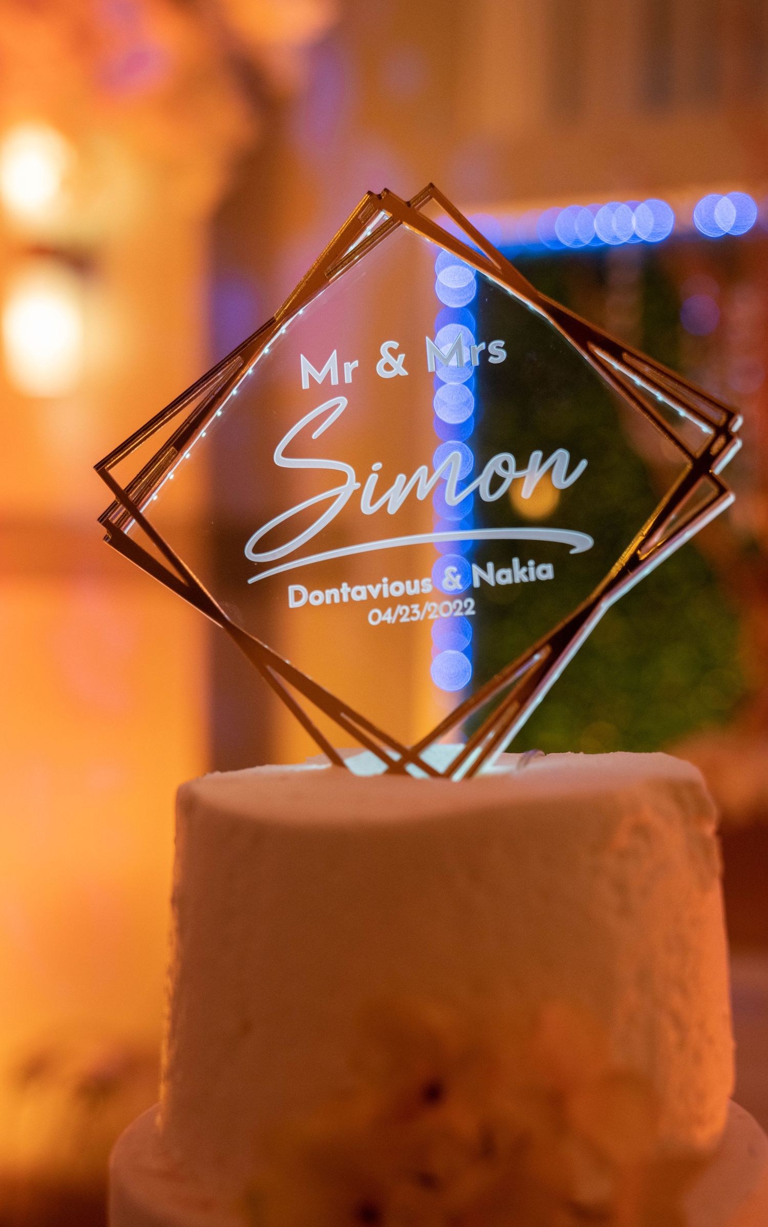 Illuminated acrylic wedding cake toppers with names displayed in elegant typography against a warm glowing background.
