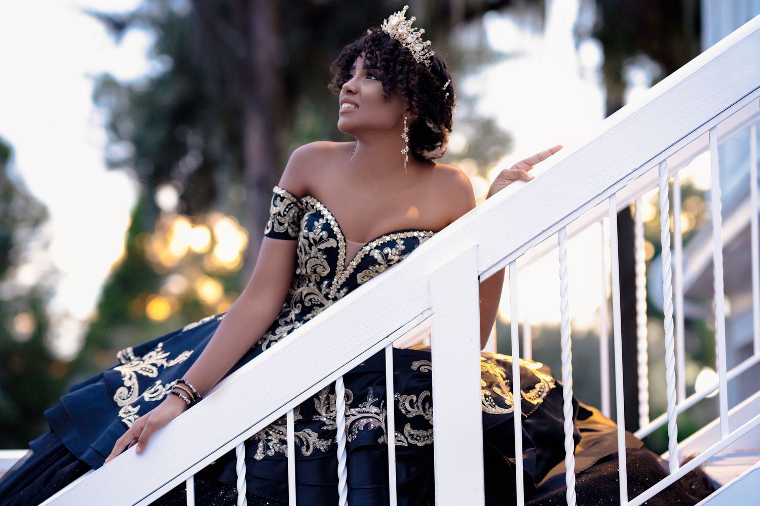 Graduate in formal attire poses on white staircase during sunset photoshoot.
