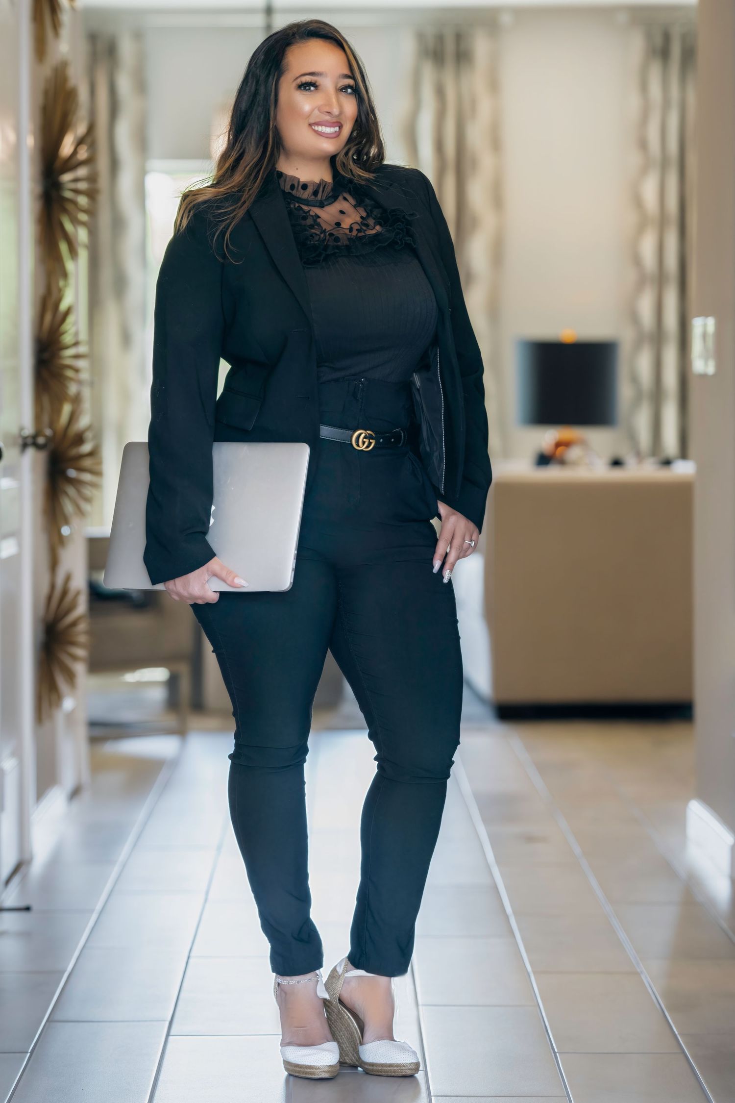 Woman in professional attire walks through modern hallway with tiled flooring and neutral decor.