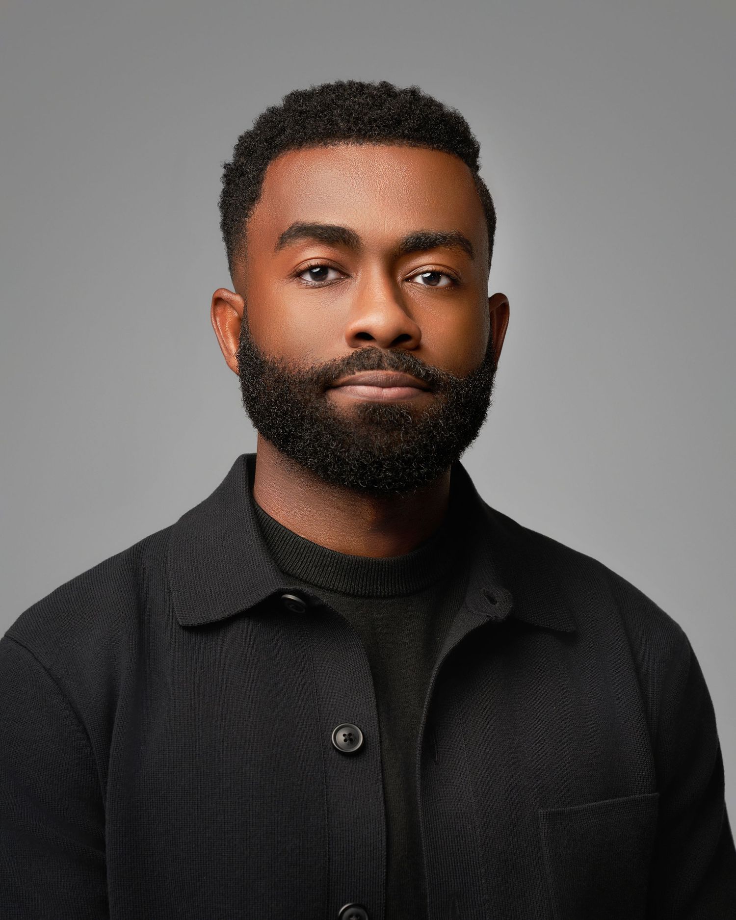 Professional headshots of a man in a black coat against a gray studio background.