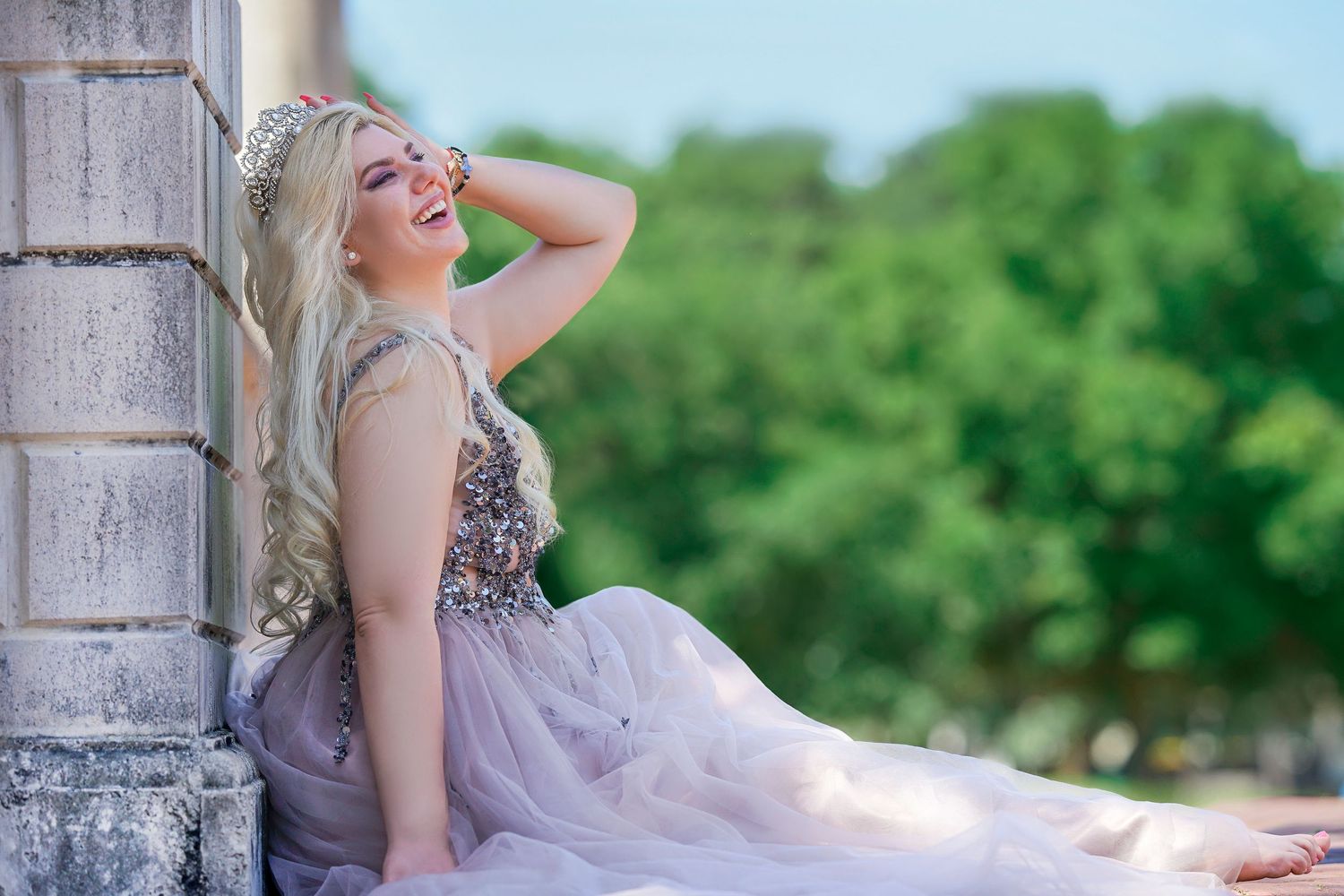 Person in flowing dress poses dramatically against stone column with green scenery in background.