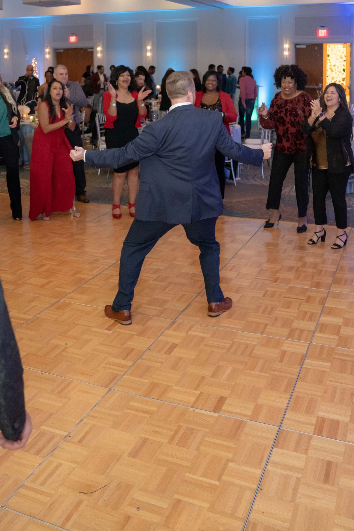 People dancing on a parquet floor at a formal event with blue lighting and red decor visible in the background.