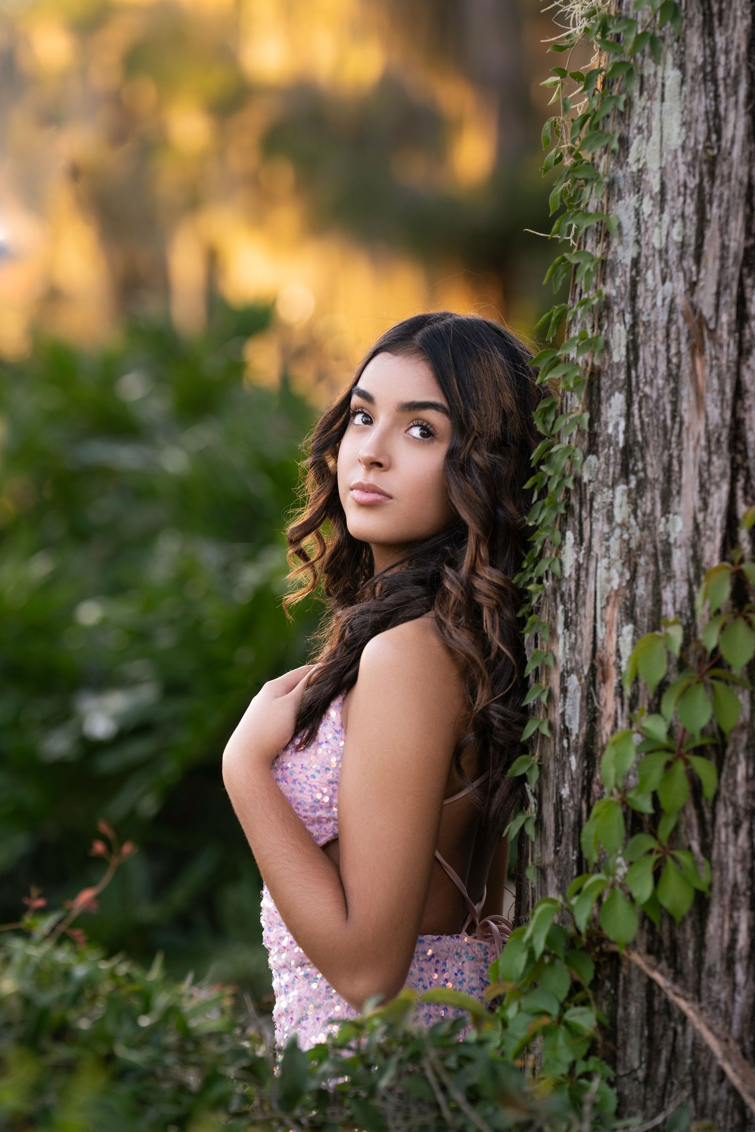 Outdoor portrait against a tree trunk with soft golden lighting and natural foliage.