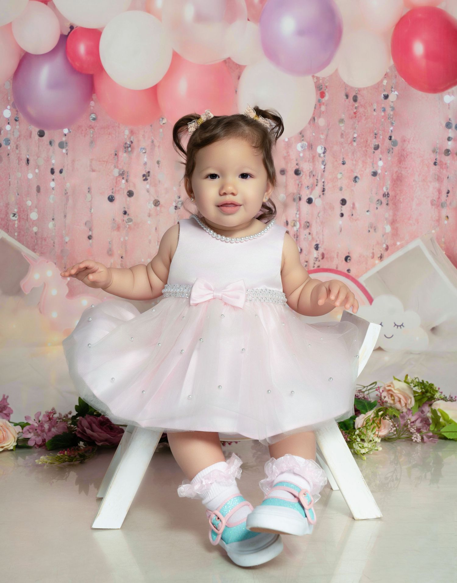 Little girl sitting on a white chair with colorful balloons in the background