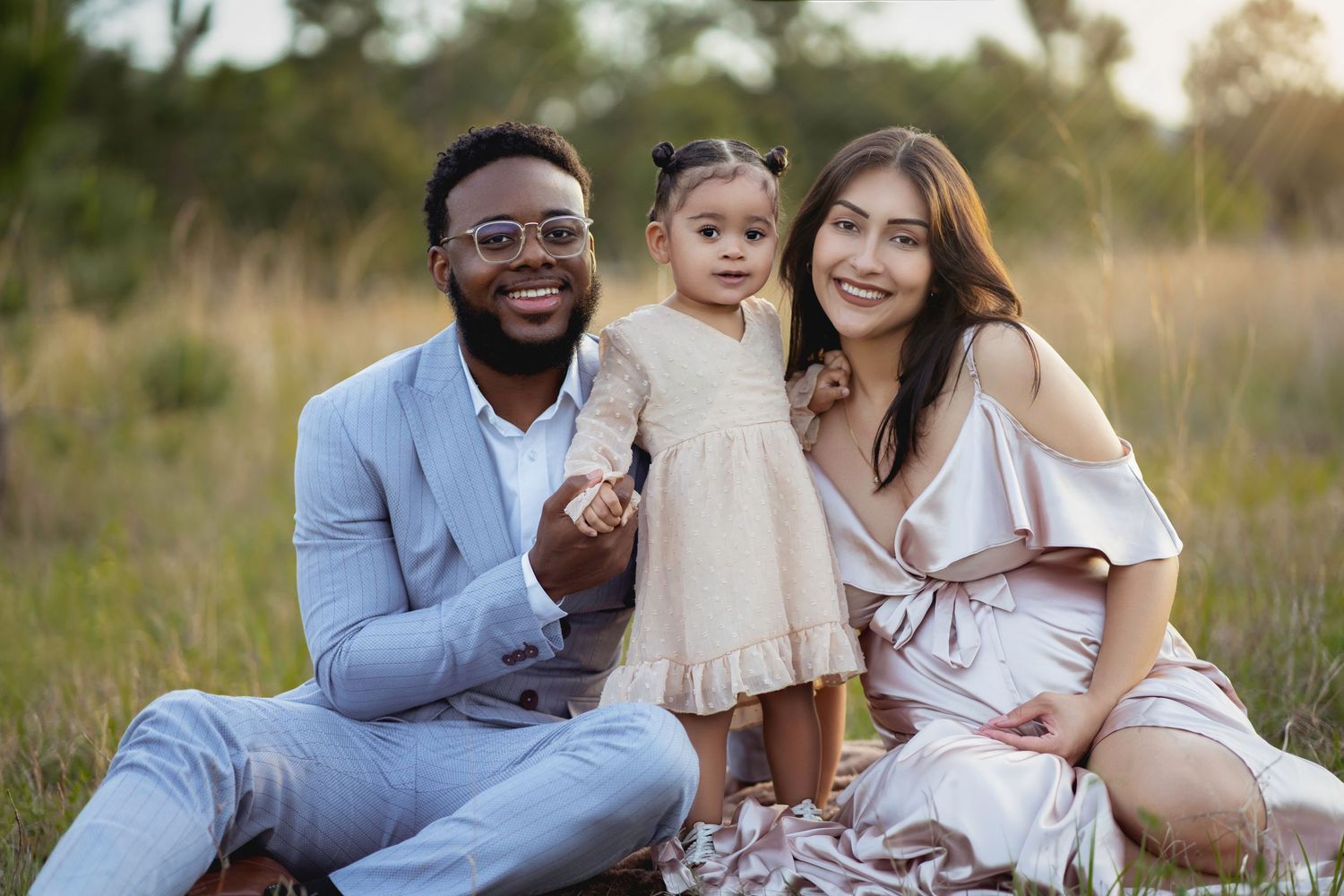A happy family poses together outdoors in a field during golden hour sunset for a professional photo session.