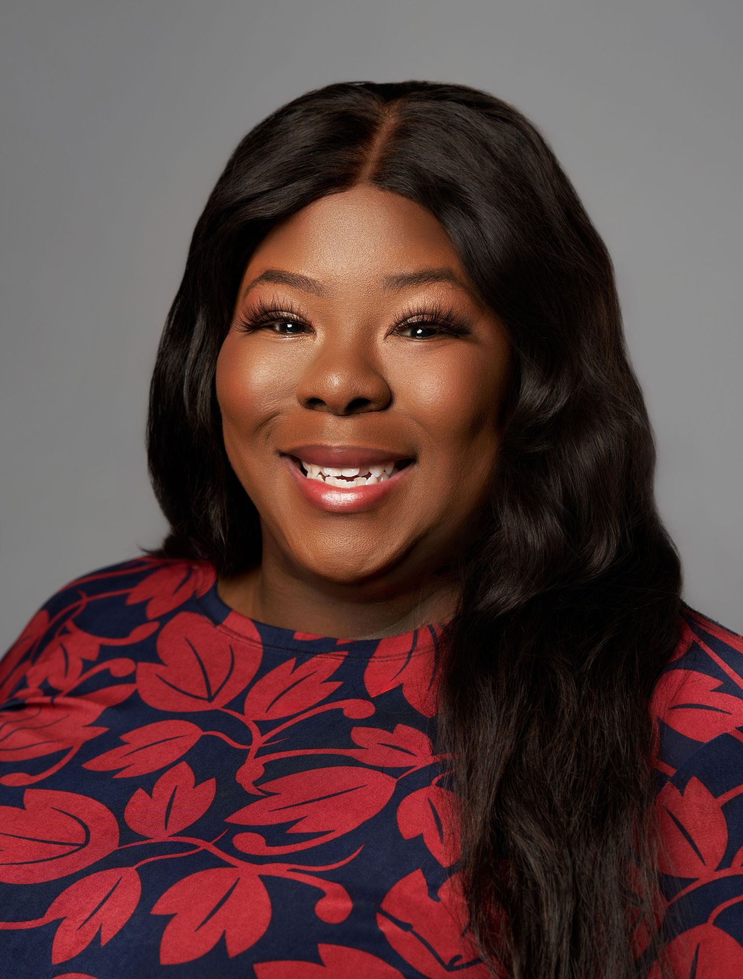 Professional headshots of a woman in a navy and red floral print top against a gray backdrop.