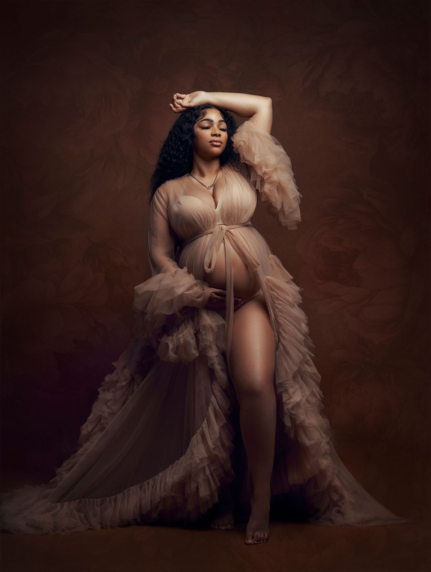 Artistic maternity photoshoot featuring flowing beige tulle fabric against a dark brown backdrop.