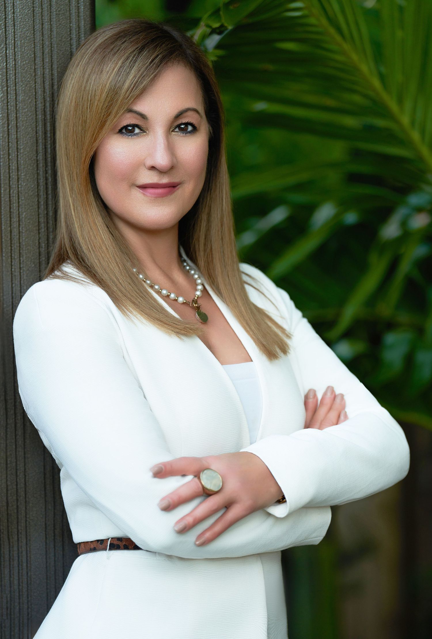 Professional headshots of person in white blazer against tropical plant background.