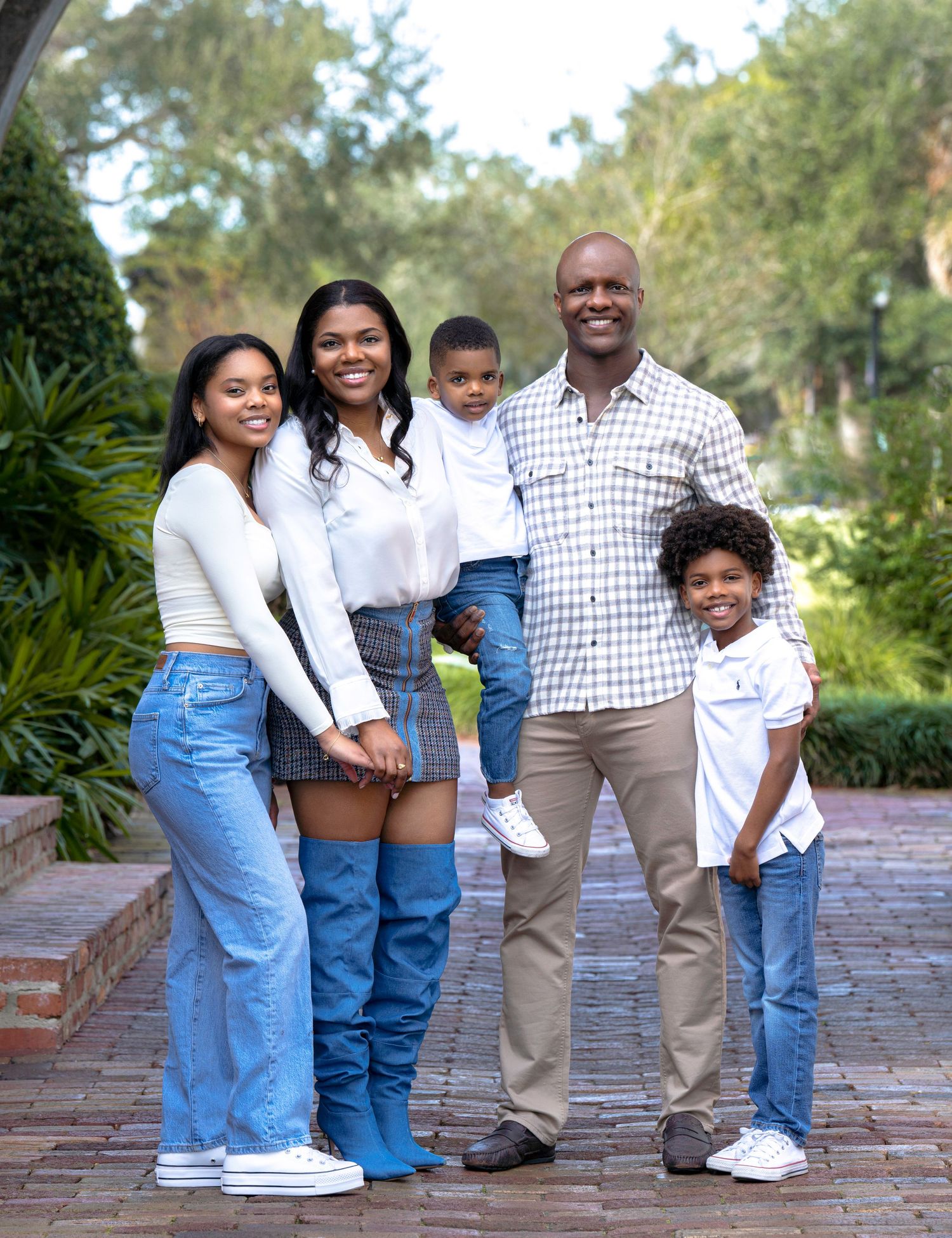 Casual family photo of five people standing together outdoors in coordinated outfits.