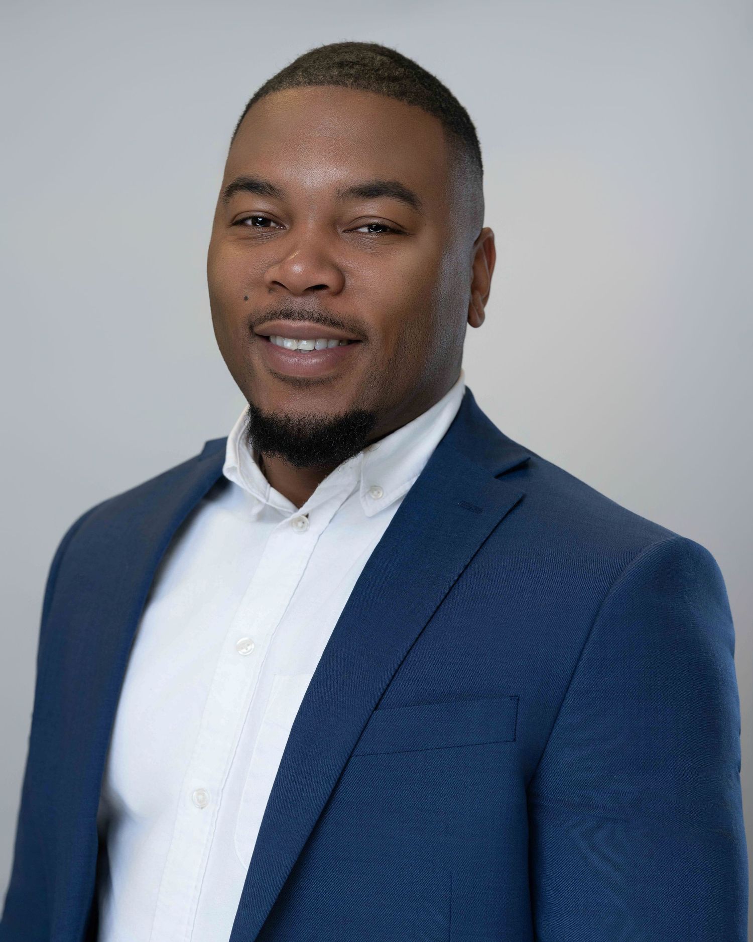 Professional headshot of someone wearing a navy suit and white dress shirt against a light gray background.