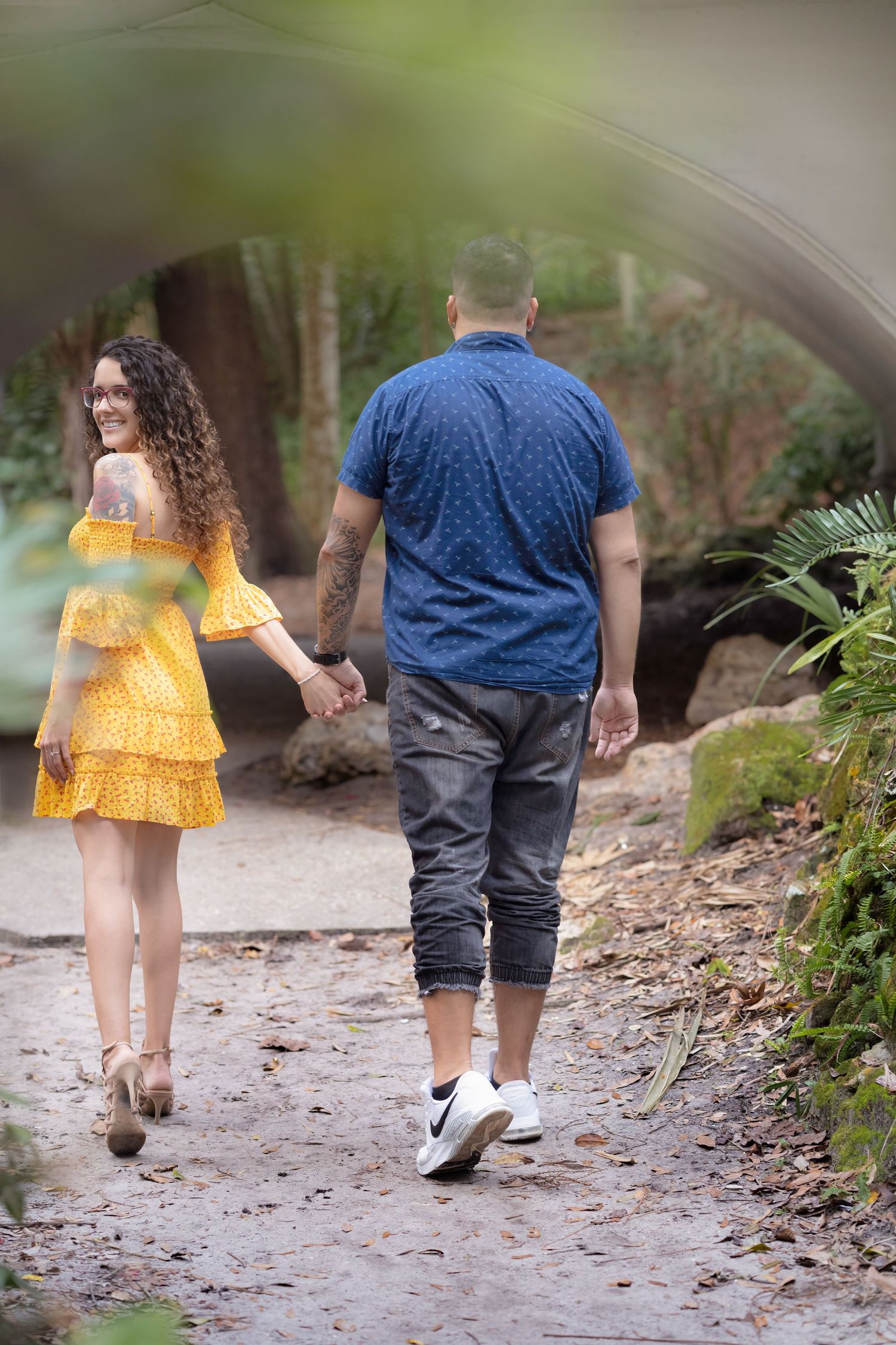 Two people walk hand in hand down a forest path wearing yellow dress and blue shirt on a summer day.