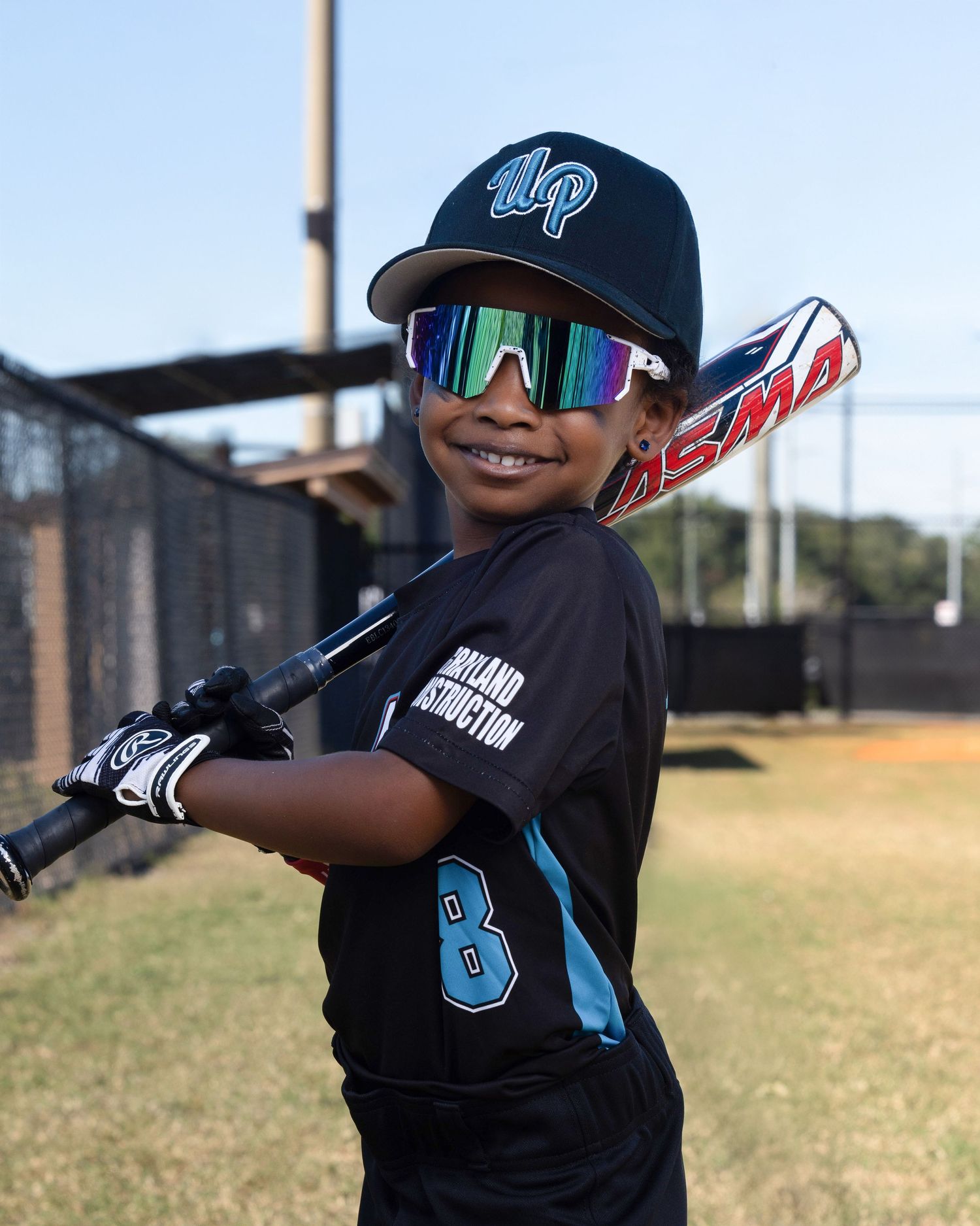 Young baseball player in black uniform takes batting stance at practice field on sunny day.