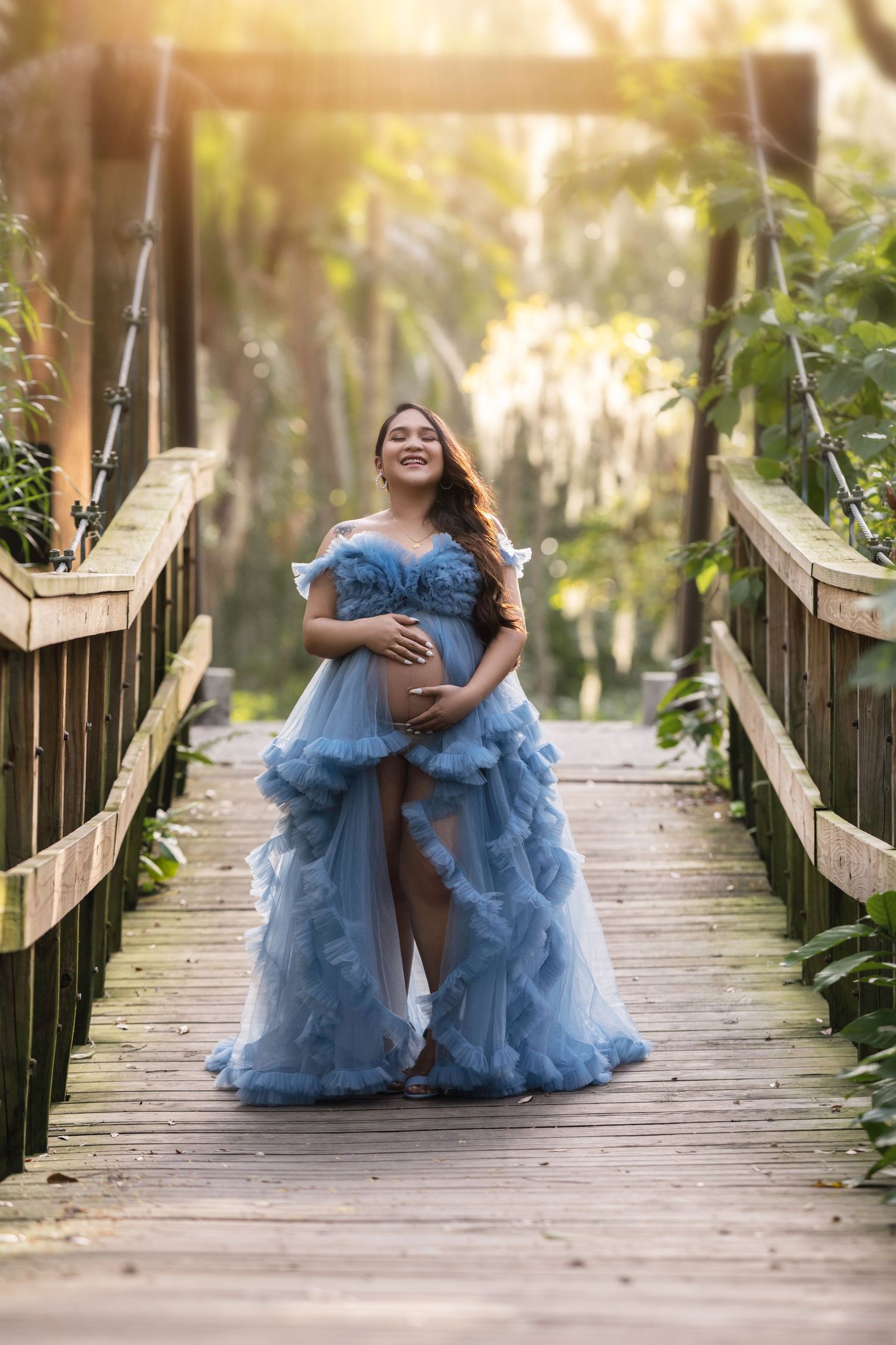 Maternity photos on a wooden boardwalk with person wearing flowing blue tulle dress.